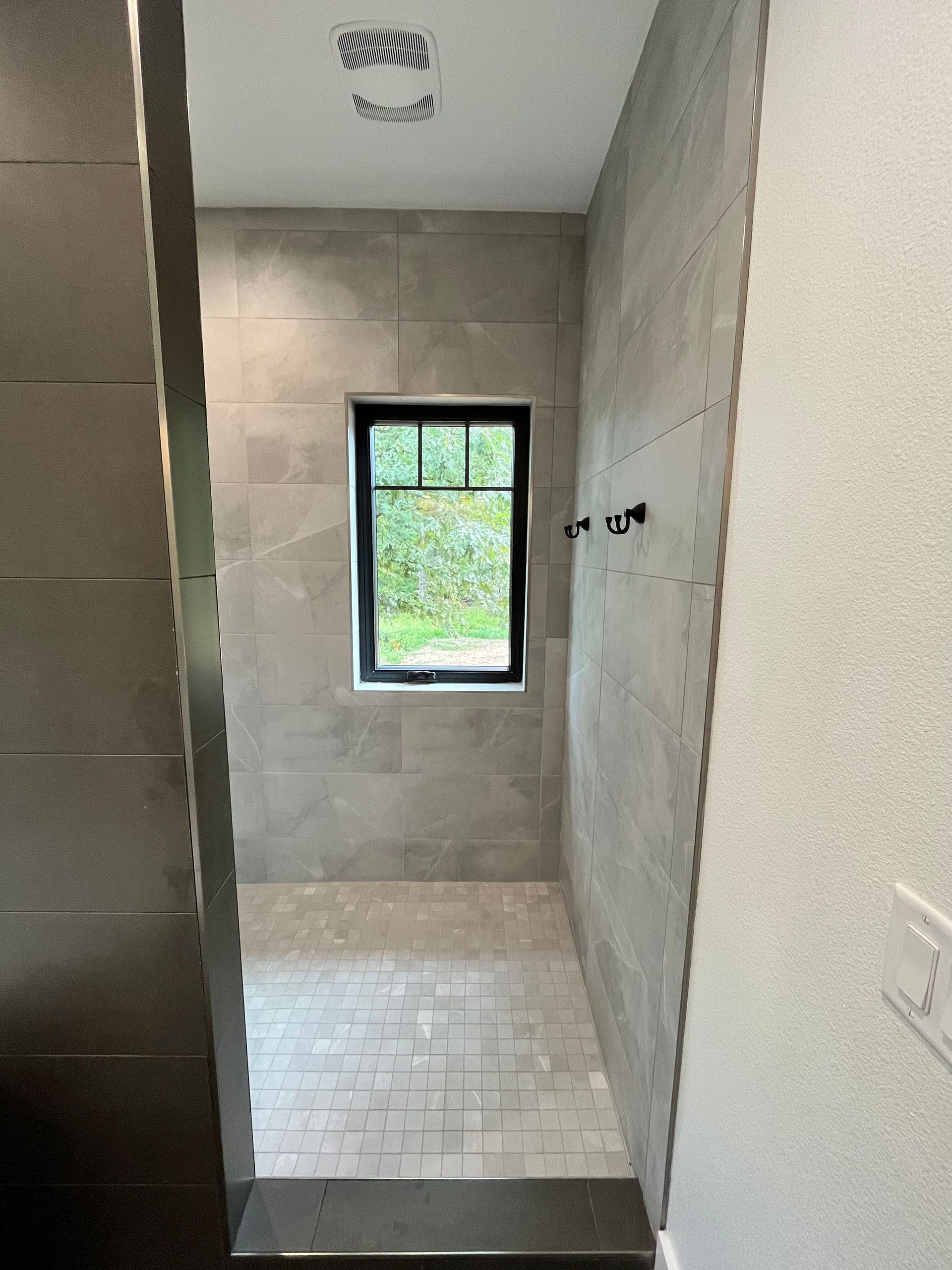 Narrow tiled shower stall with a small window and unfinished concrete walls