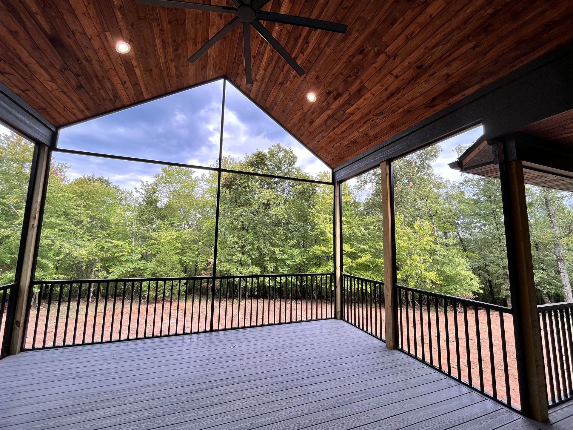 Covered deck with black railings, wood ceiling, and treetop view through screened walls.