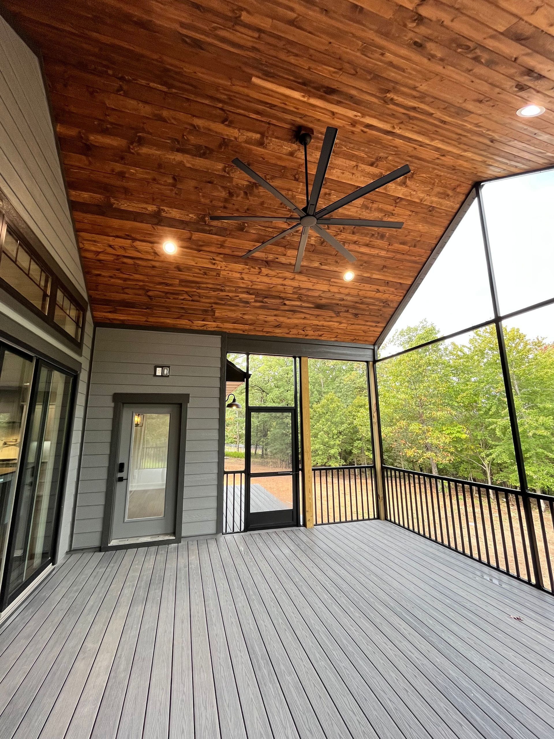 Covered screened porch with wood ceiling, black ceiling fan, gray floor, and large mesh windows overlooking trees