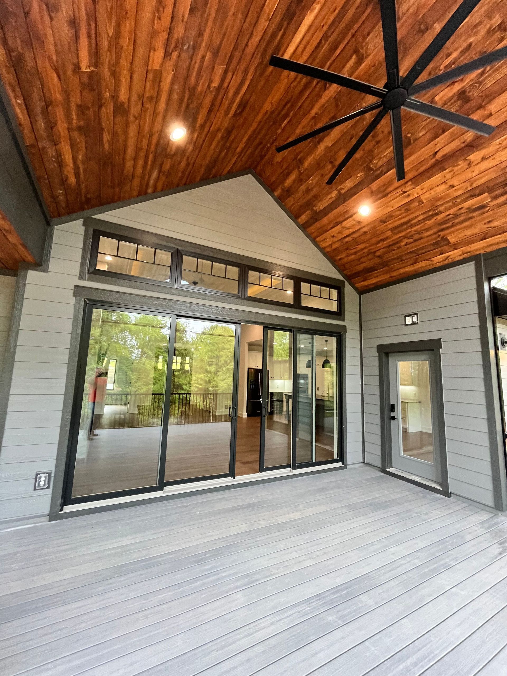 Covered patio with wood ceiling, black ceiling fan, glass doors, and gray tiled floor.