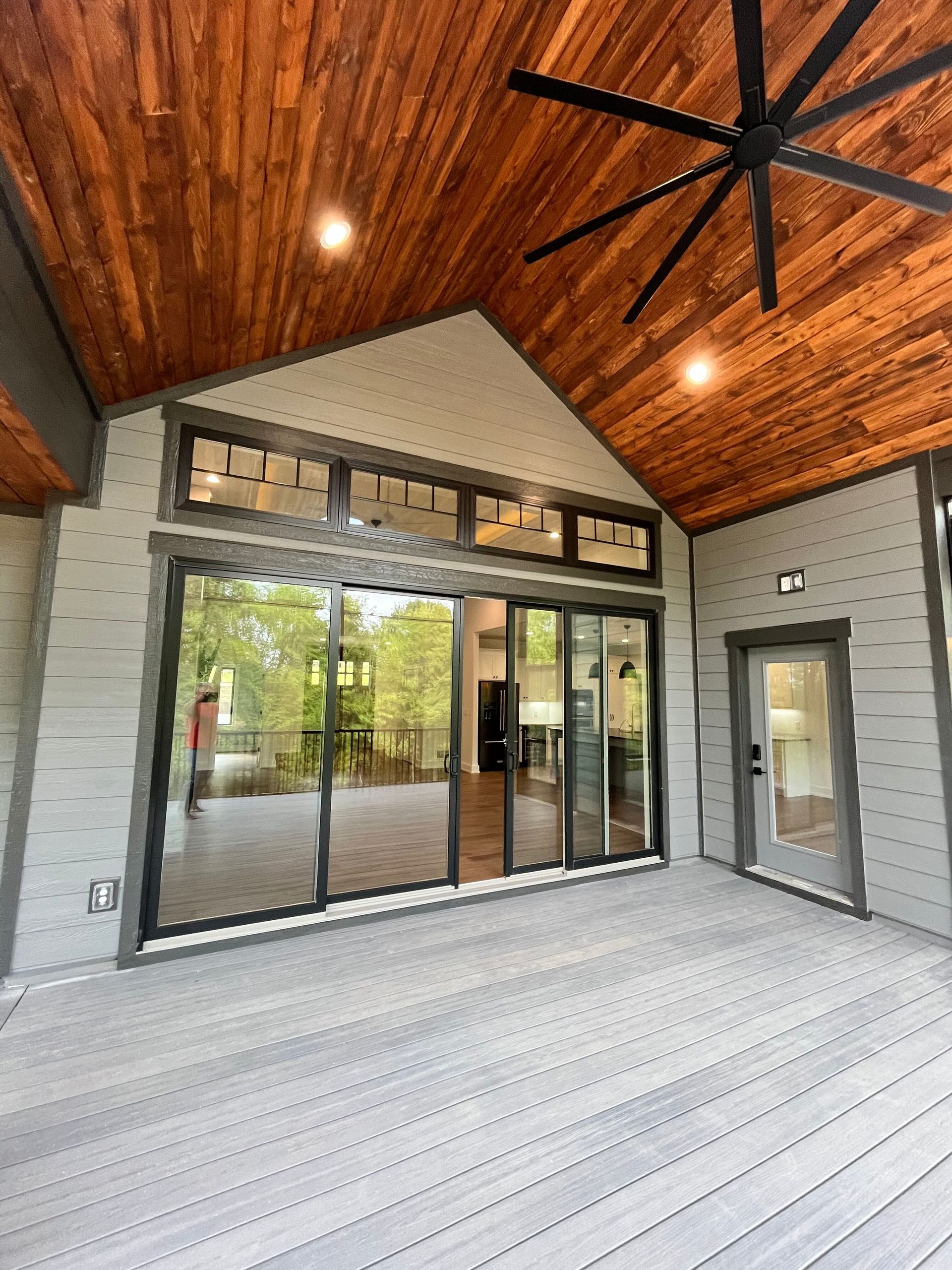 Covered patio with wood ceiling, large sliding glass doors, and gray brick walls.