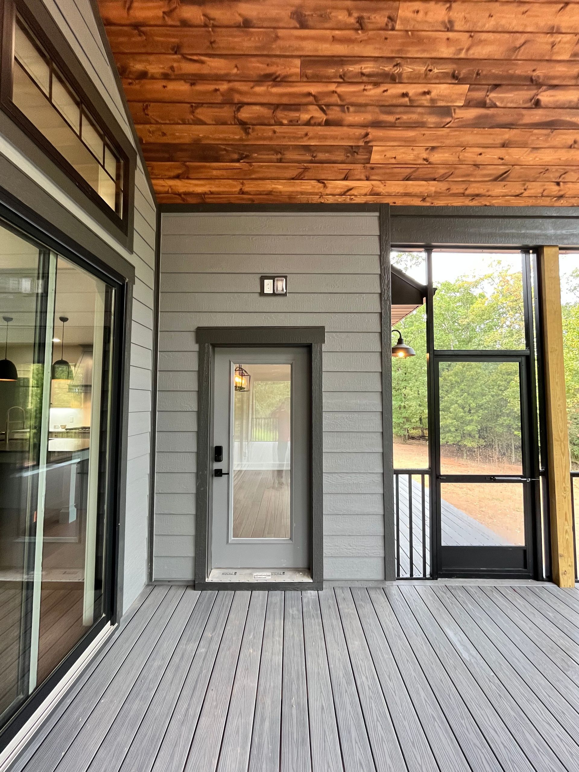 Covered porch with gray door, wood ceiling, and large glass windows overlooking outdoors