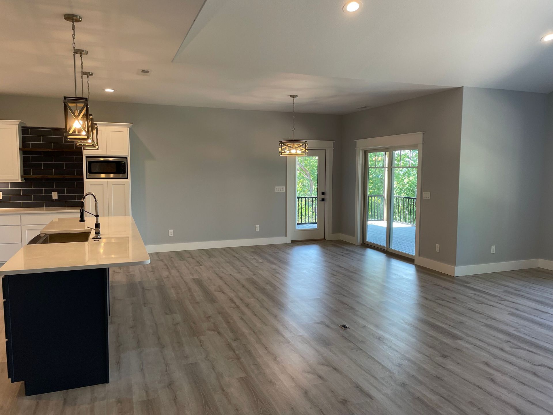 Open-plan kitchen and living room with gray walls, wood floors, pendant lights, and sliding glass doors.