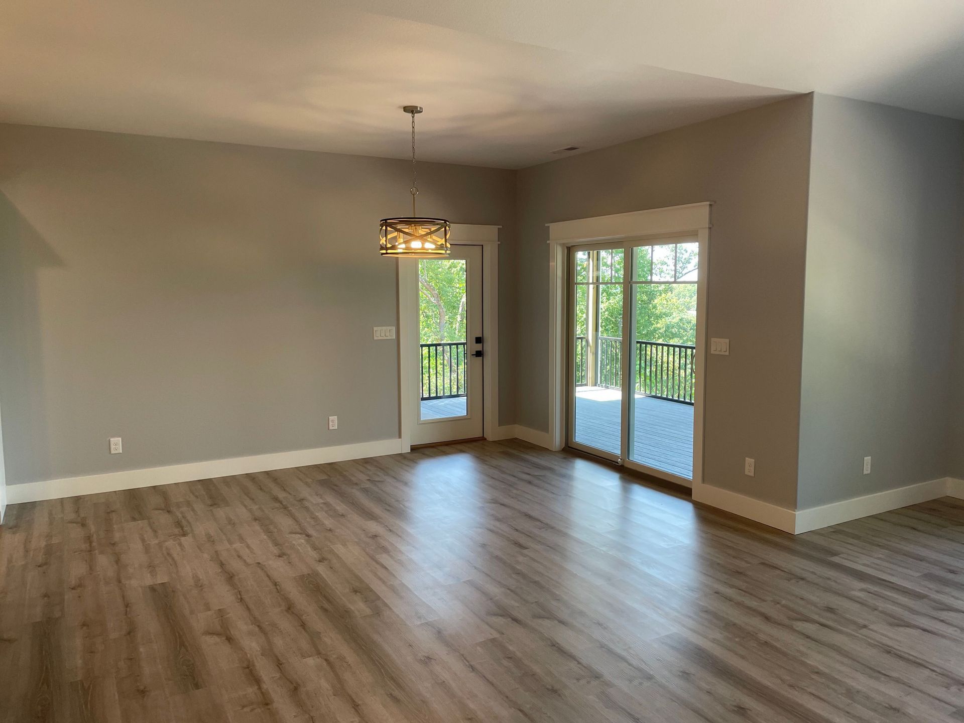 Empty living room with wood floors, beige walls, and sliding glass doors opening to a deck.