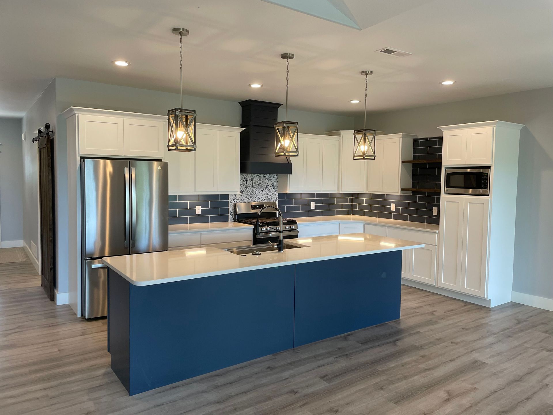 Modern kitchen with blue island, white cabinets, stainless steel appliances, and pendant lights