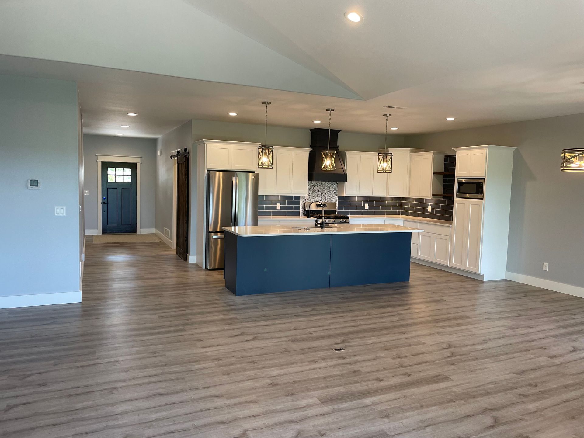 Open-plan kitchen with blue island, white cabinets, and wood-look flooring in a bright empty room