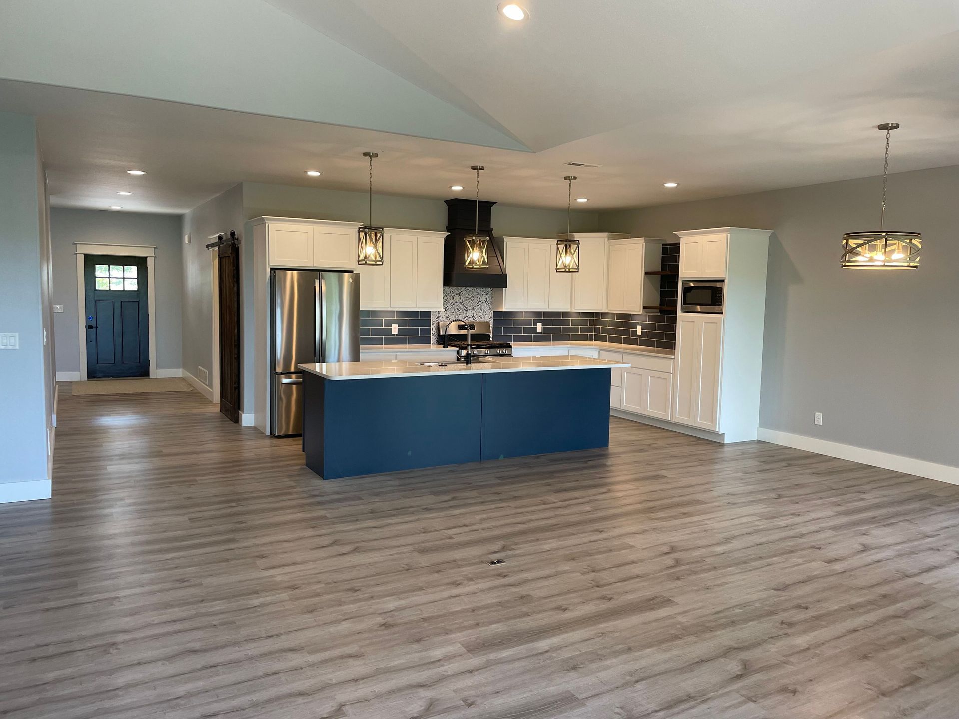 Open-concept kitchen and living area with gray floors, blue island, stainless fridge, and pendant light