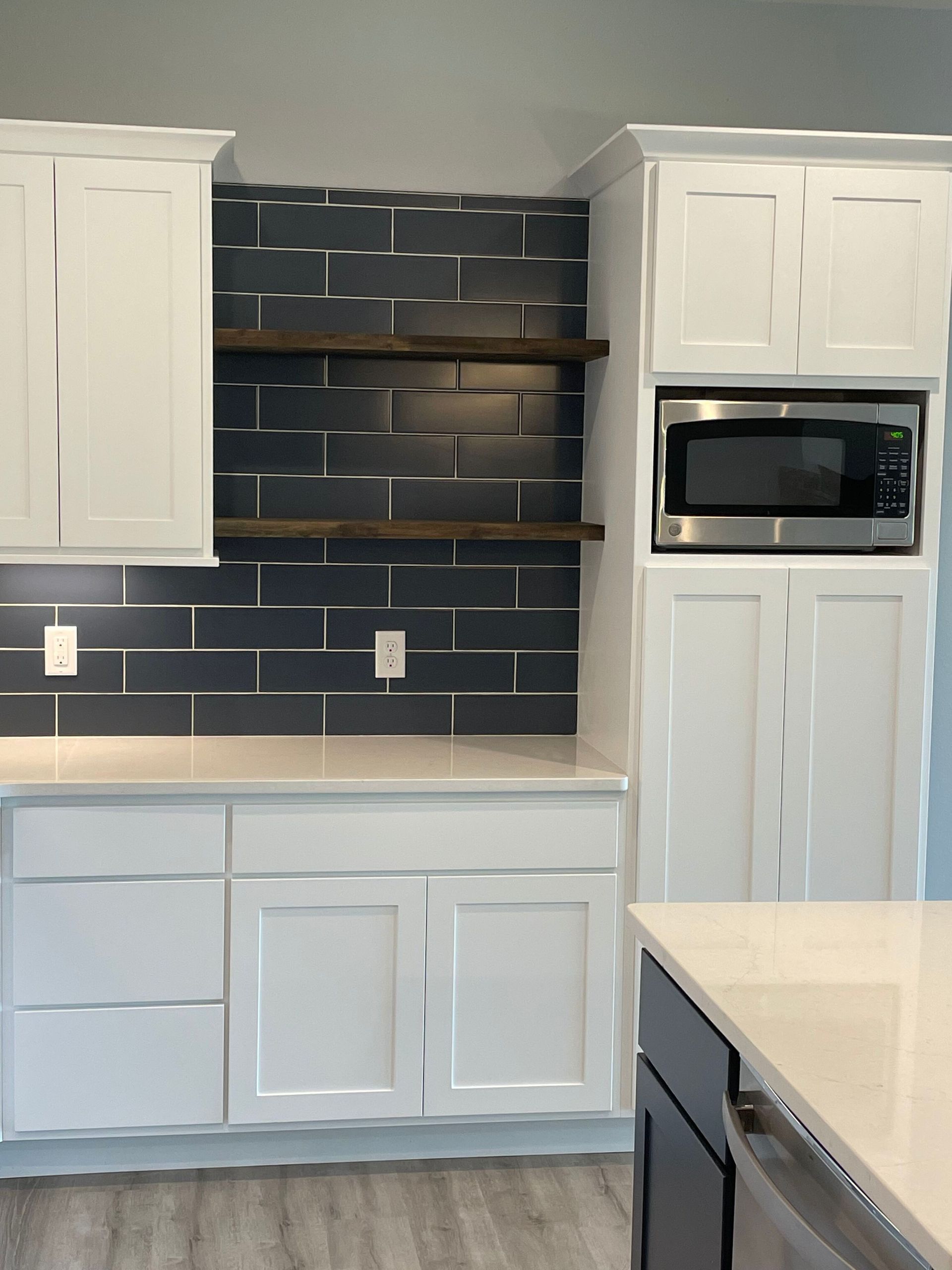 Modern kitchen with white cabinets, dark blue tile backsplash, open shelves, and built-in microwave