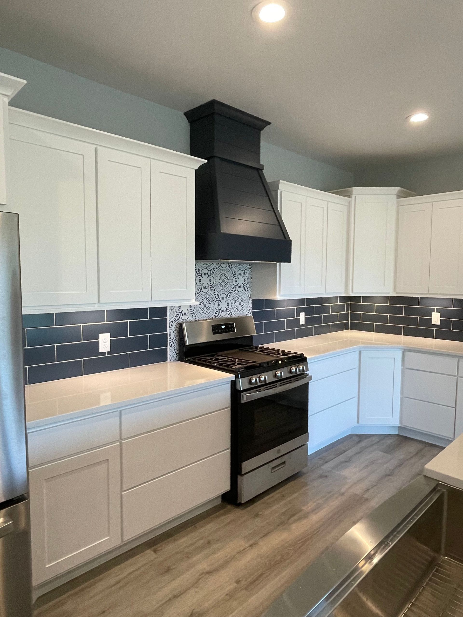 Modern kitchen with white cabinets, black range hood, gray backsplash, and stainless steel stove and fridge
