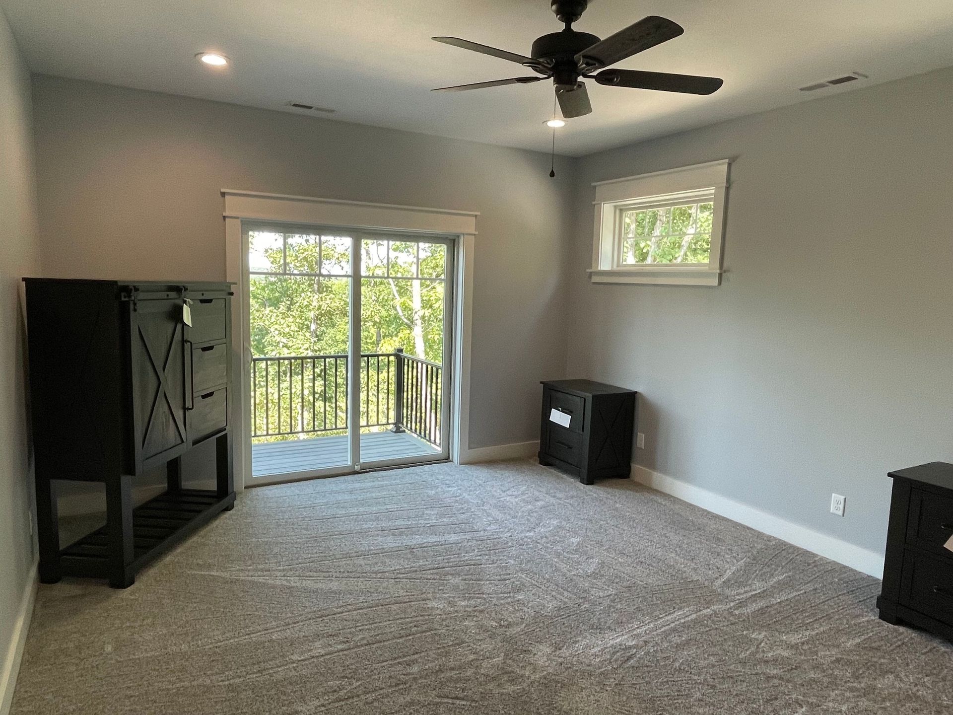 Empty carpeted living room with ceiling fan, sliding glass doors, and a small window.