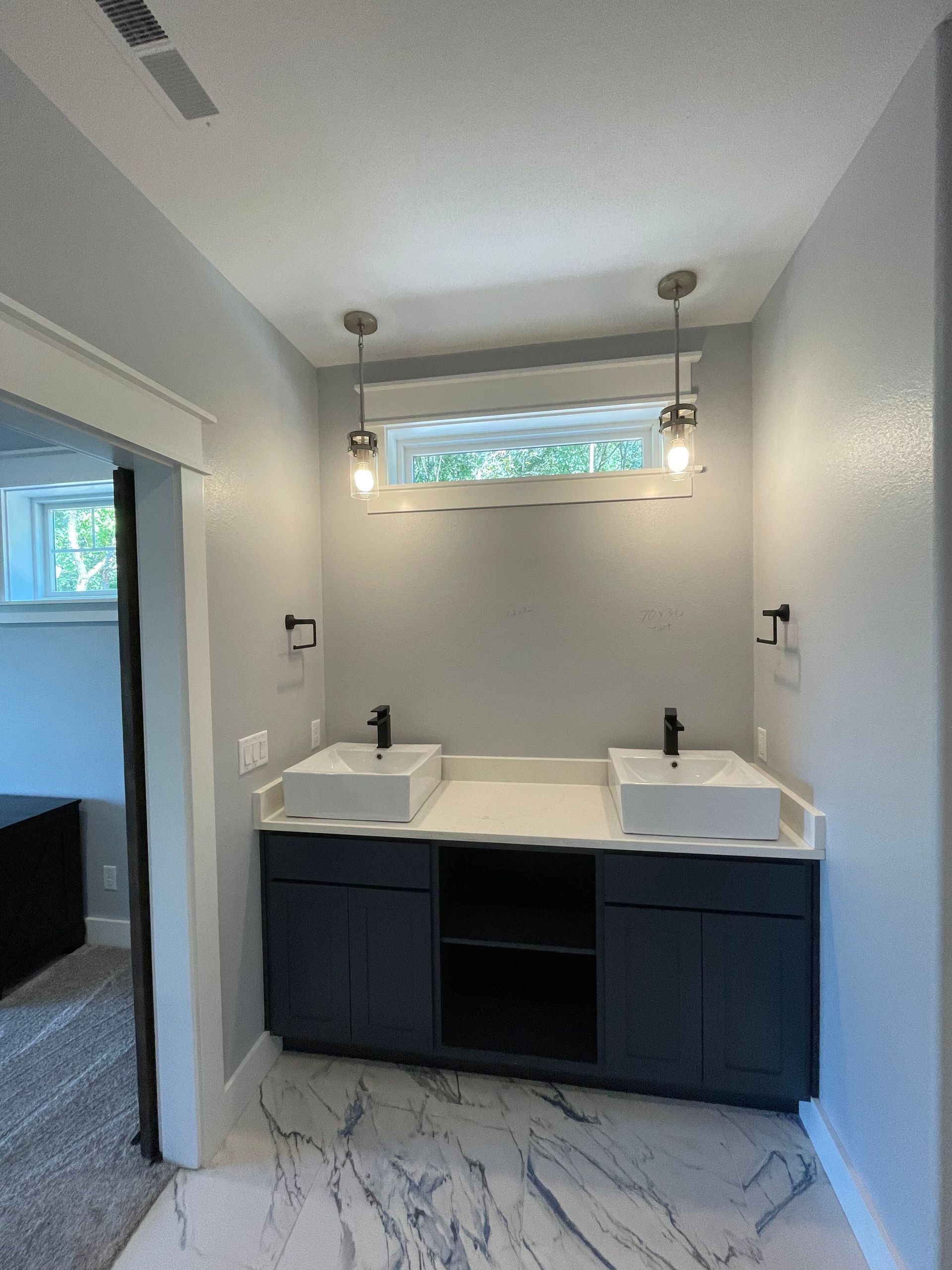 Modern bathroom vanity with double sinks, dark cabinets, and a small window above the mirror.