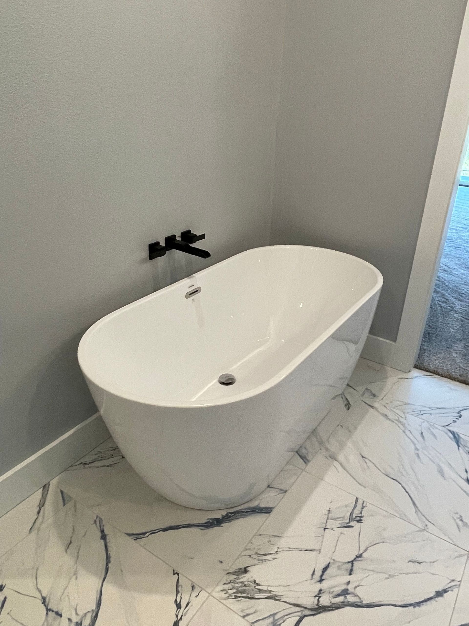 Modern freestanding white bathtub in a tiled bathroom with a wall-mounted black faucet