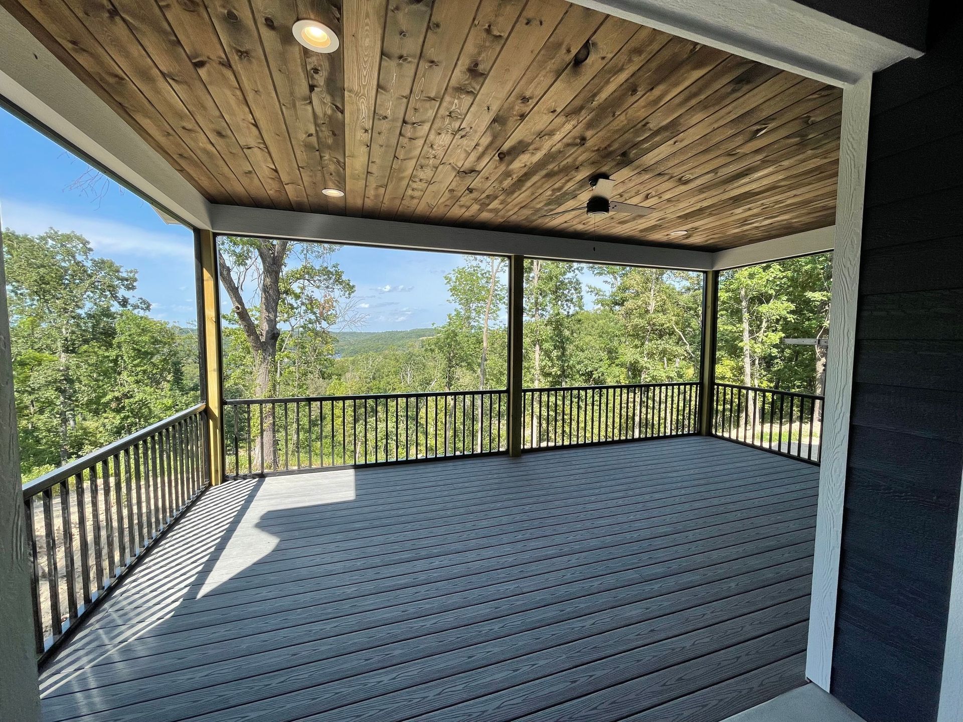 Covered wooden porch with gray floorboards, railing, and forest mountain view beyond.