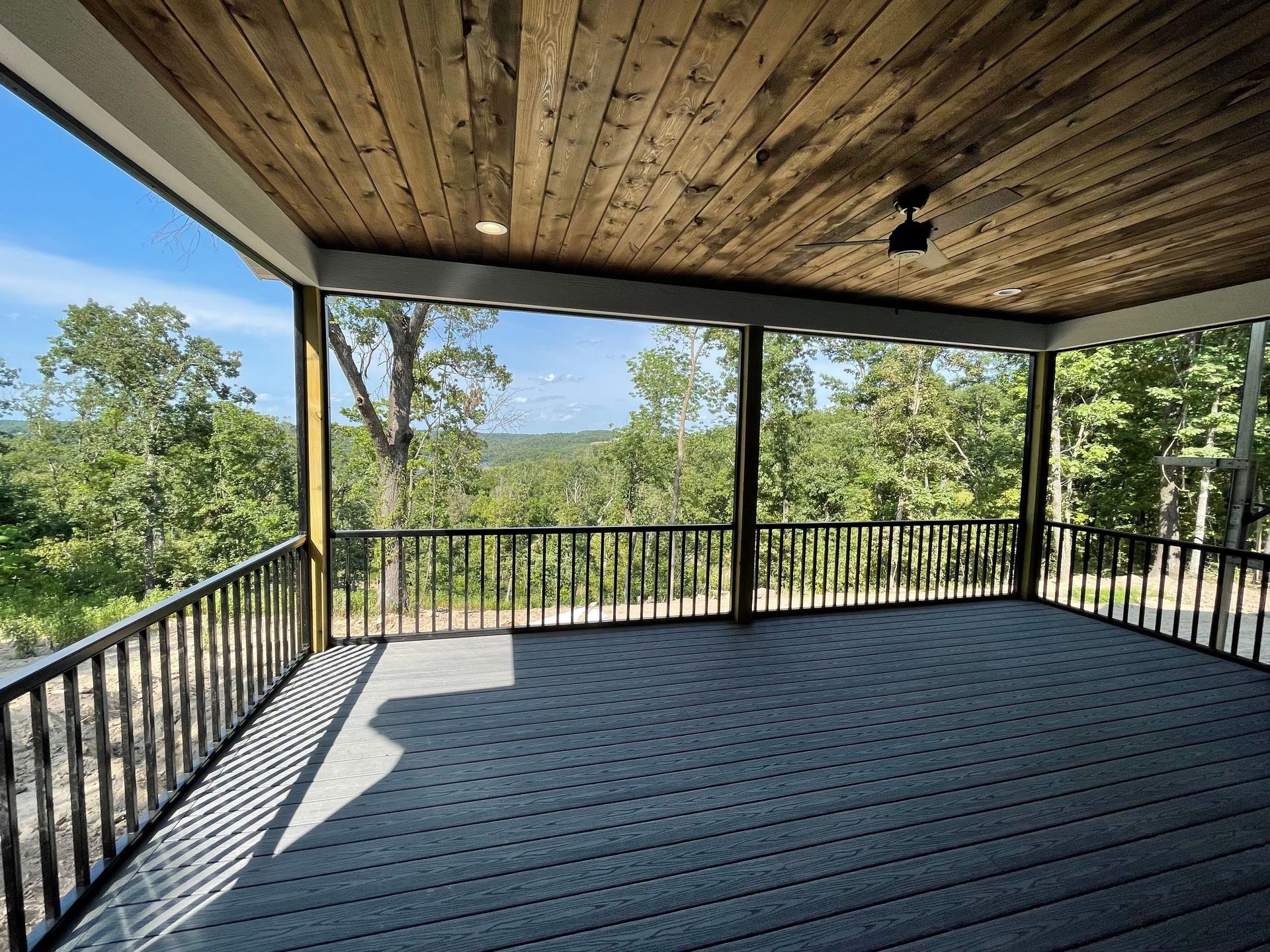 Covered outdoor deck with black railing, wood ceiling, and forest view