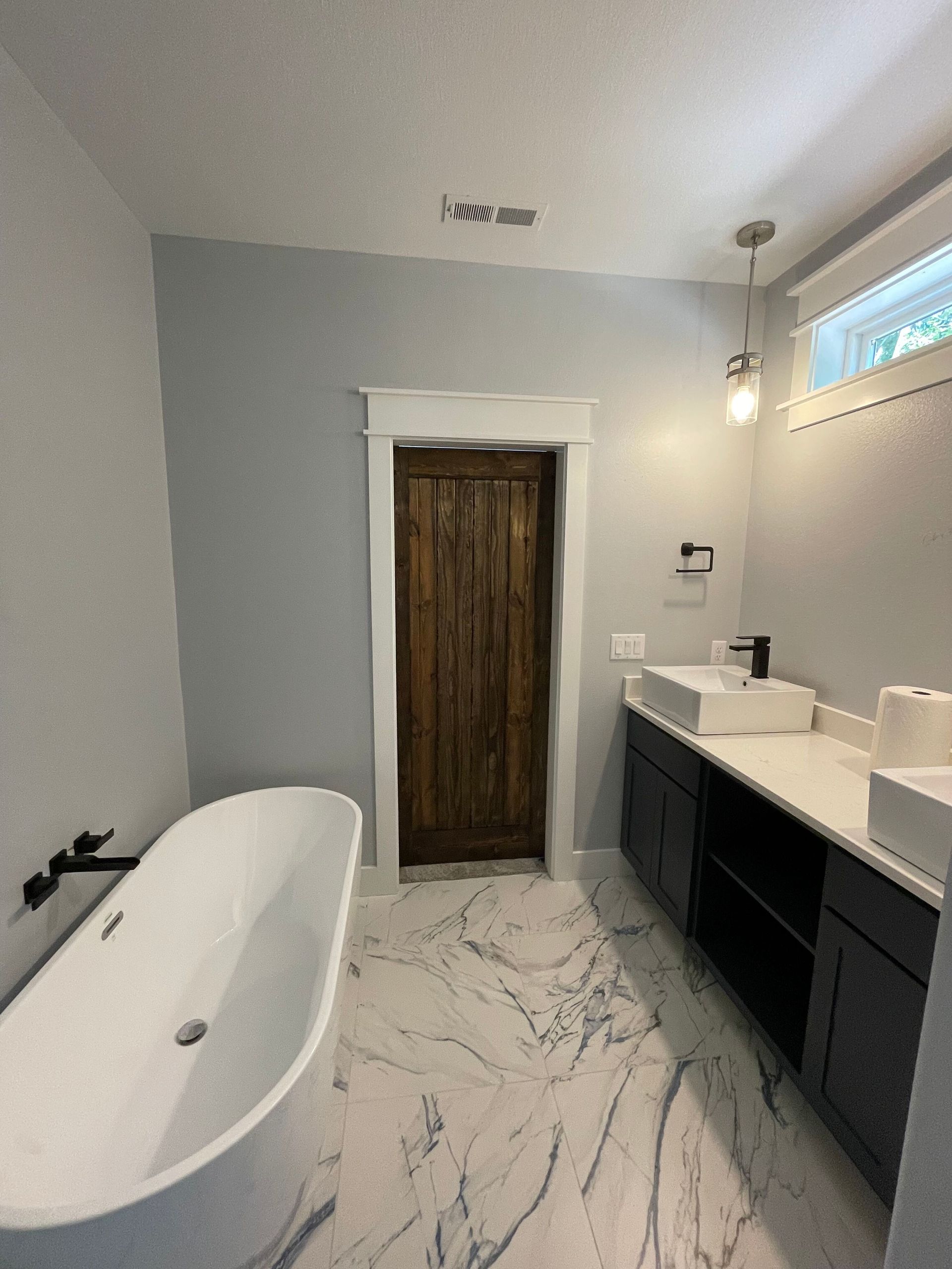 Modern bathroom with freestanding tub, double vanity, marble floor, and wooden door in the center