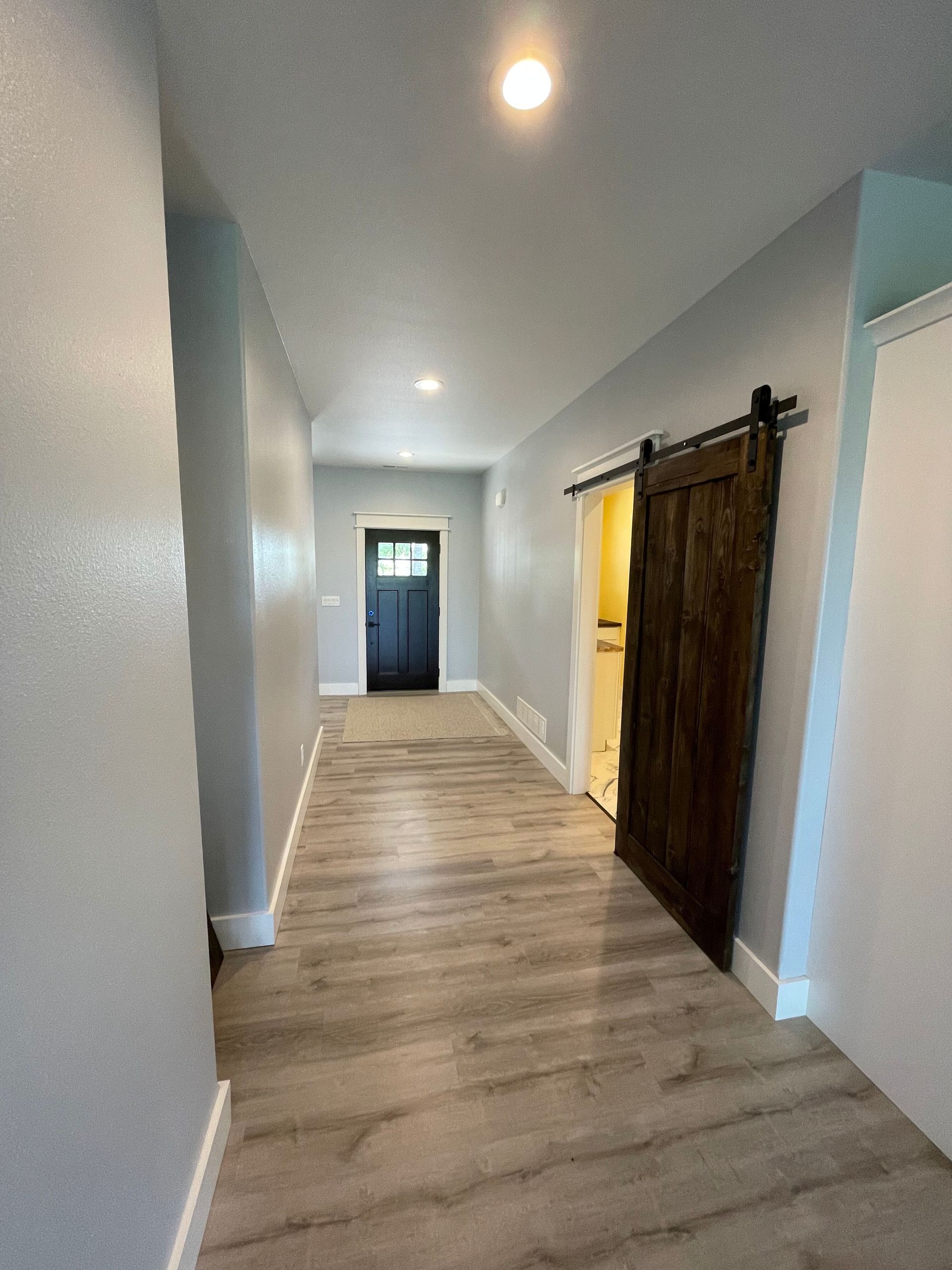 Long hallway with light walls, wood floor, recessed lights, and a dark barn door on the right