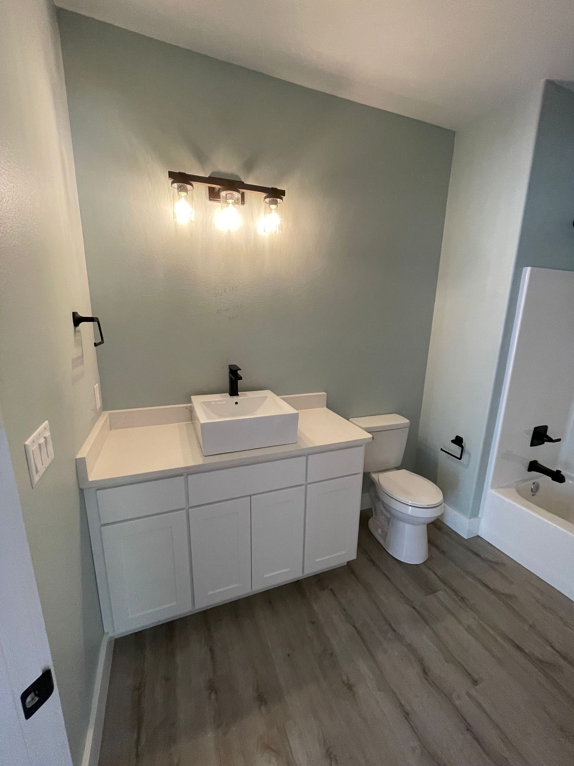 Modern bathroom with white vanity, lit mirror, toilet, tub, and gray walls and flooring