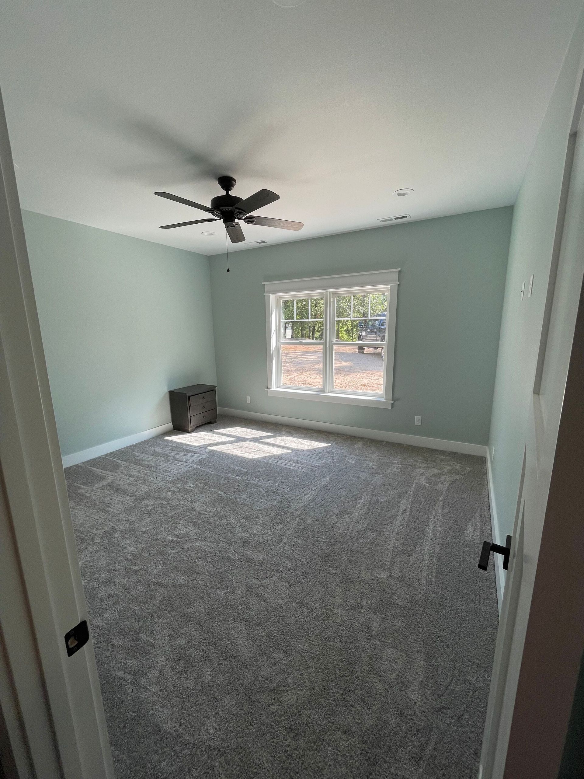 Empty carpeted bedroom with light green walls, ceiling fan, and a window letting in daylight