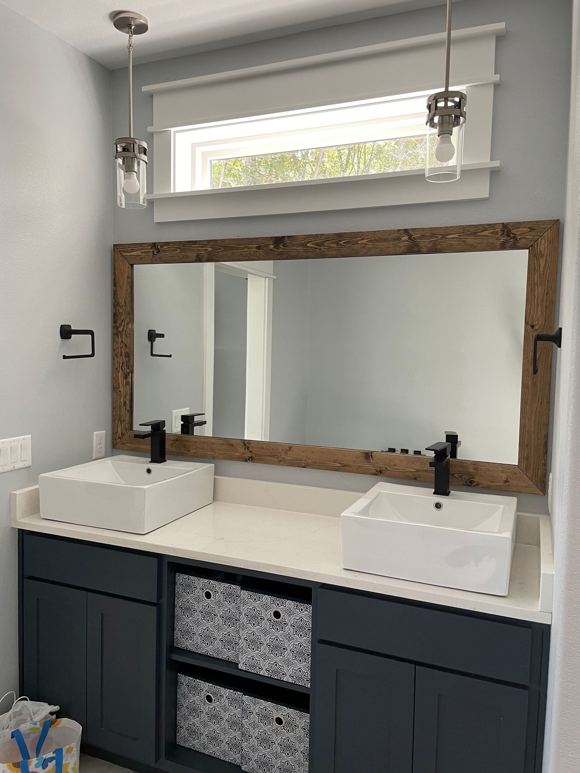 Double vanity bathroom with dark cabinets, white sinks, large rustic mirror, and a window above.