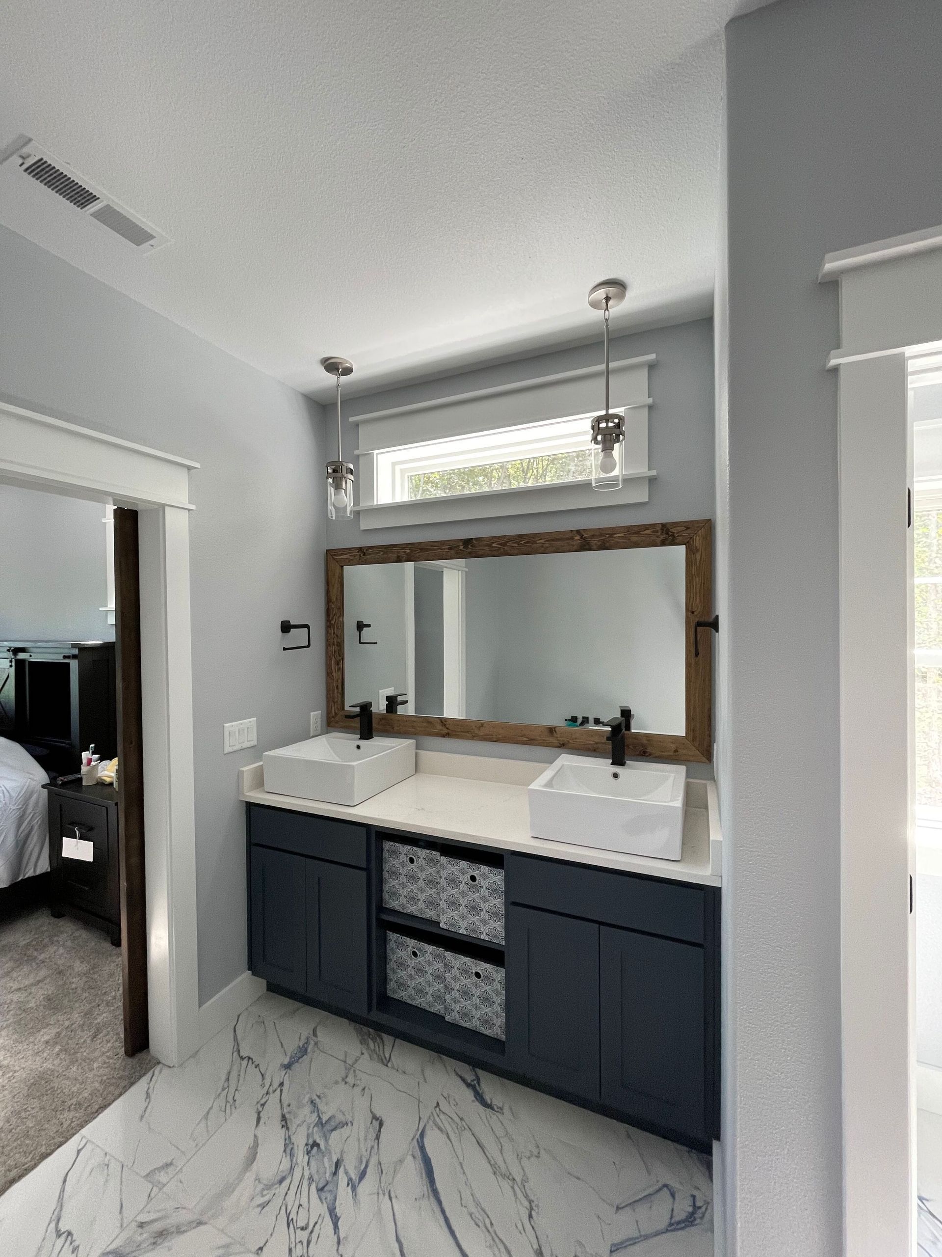 Modern bathroom with dark vanity, white countertop, large mirror, and marble-patterned floor tile.