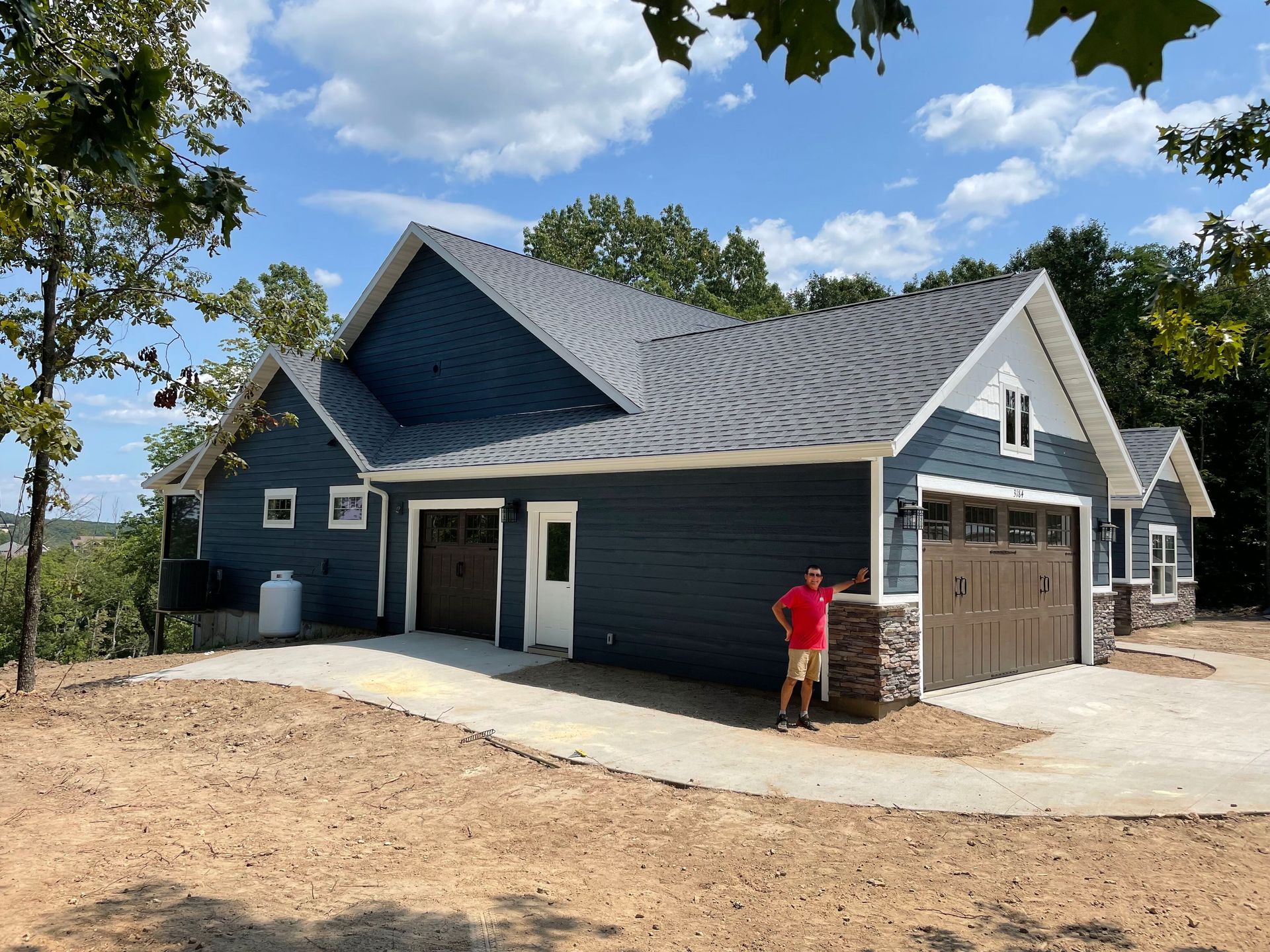 New dark blue house under construction with a person standing near the garage and unfinished dirt yard