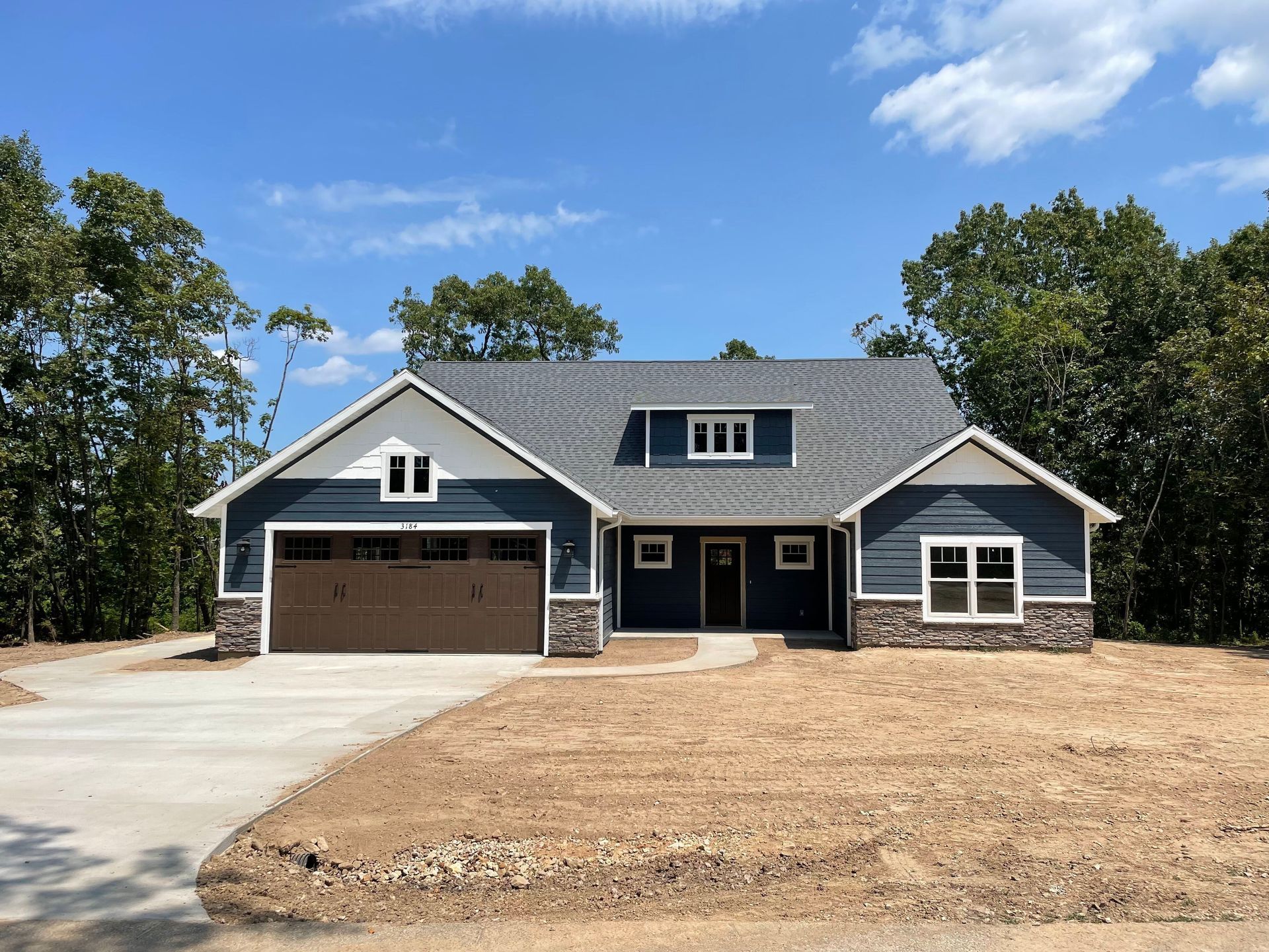 Modern single-story house with dark gray siding, stone accents, and a two-car garage under construction.