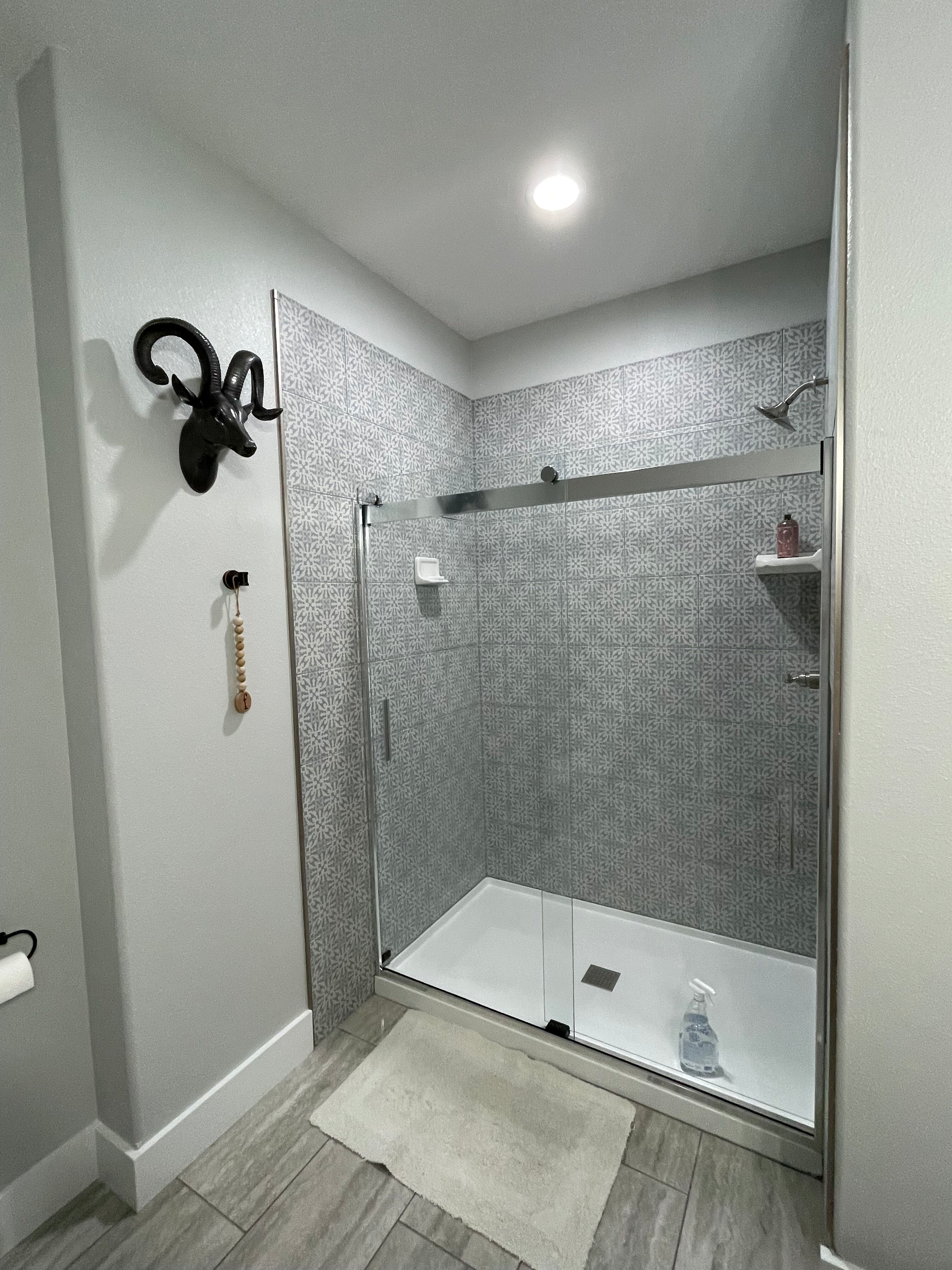 Modern walk-in shower with gray mosaic tile, glass door, and recessed ceiling light
