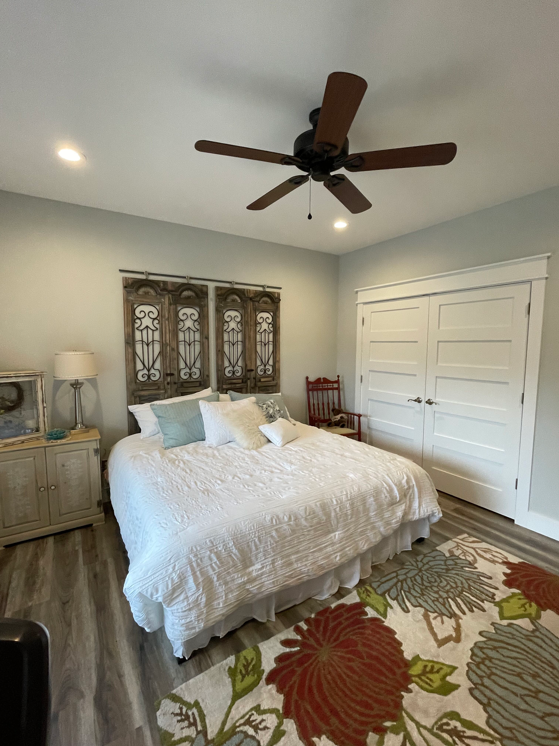 Bright bedroom with white bed, floral rug, ceiling fan, and white closet doors