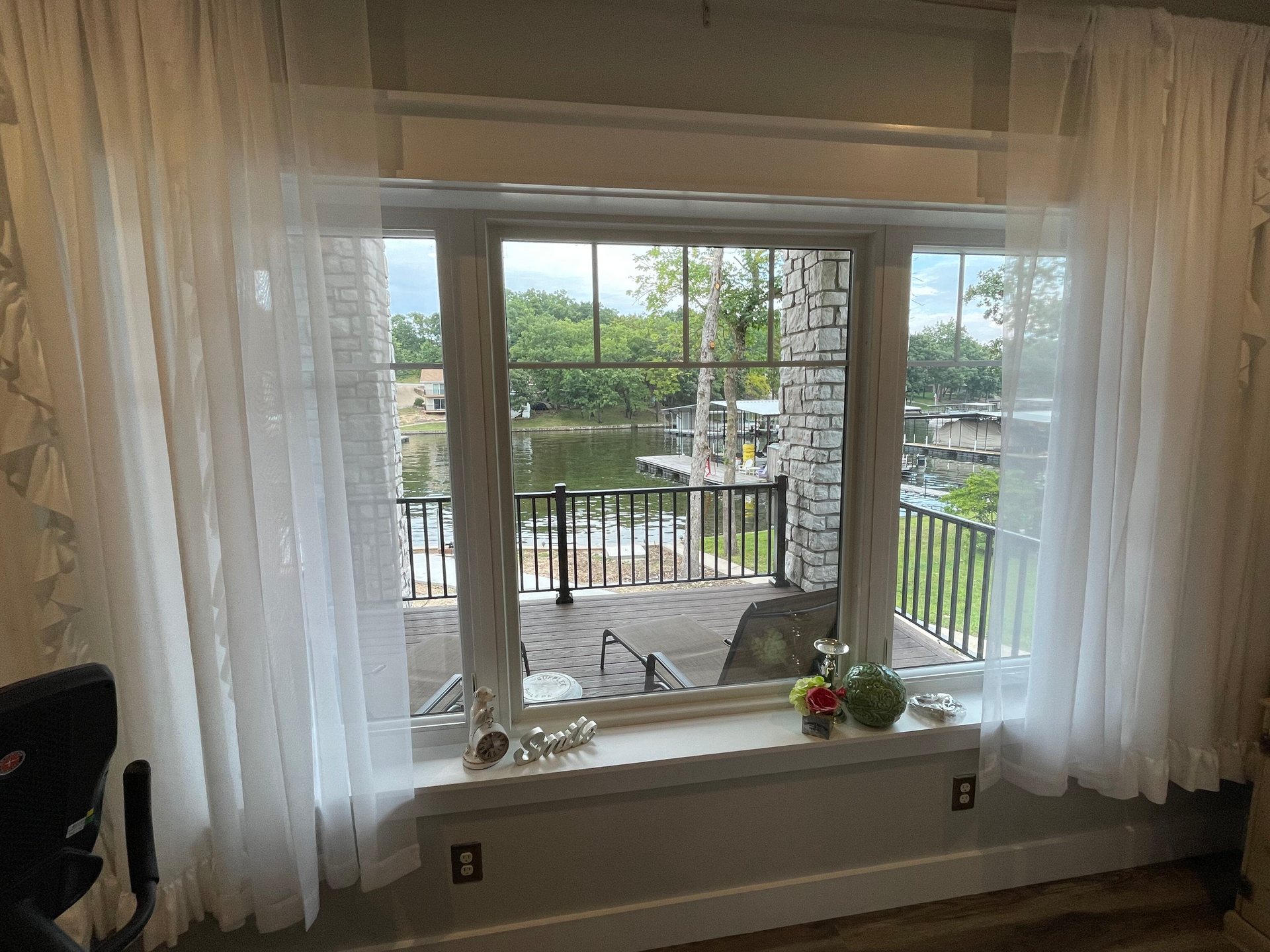 Sheer curtains framing a bay window overlooking a patio, railing, and trees.