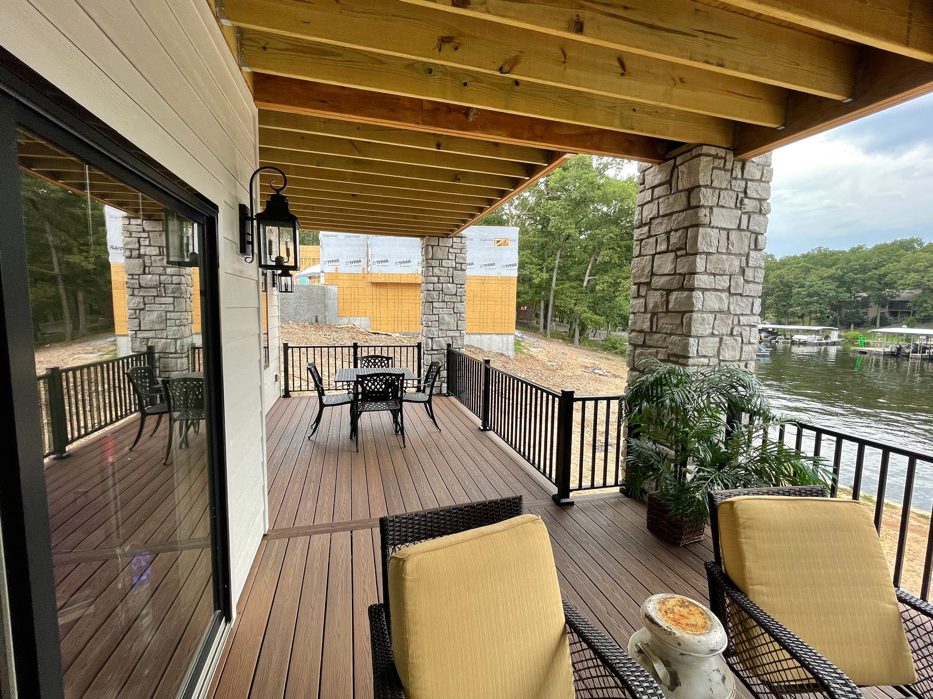 Covered patio with wooden ceiling, stone columns, lounge chairs, and a railing overlooking the water