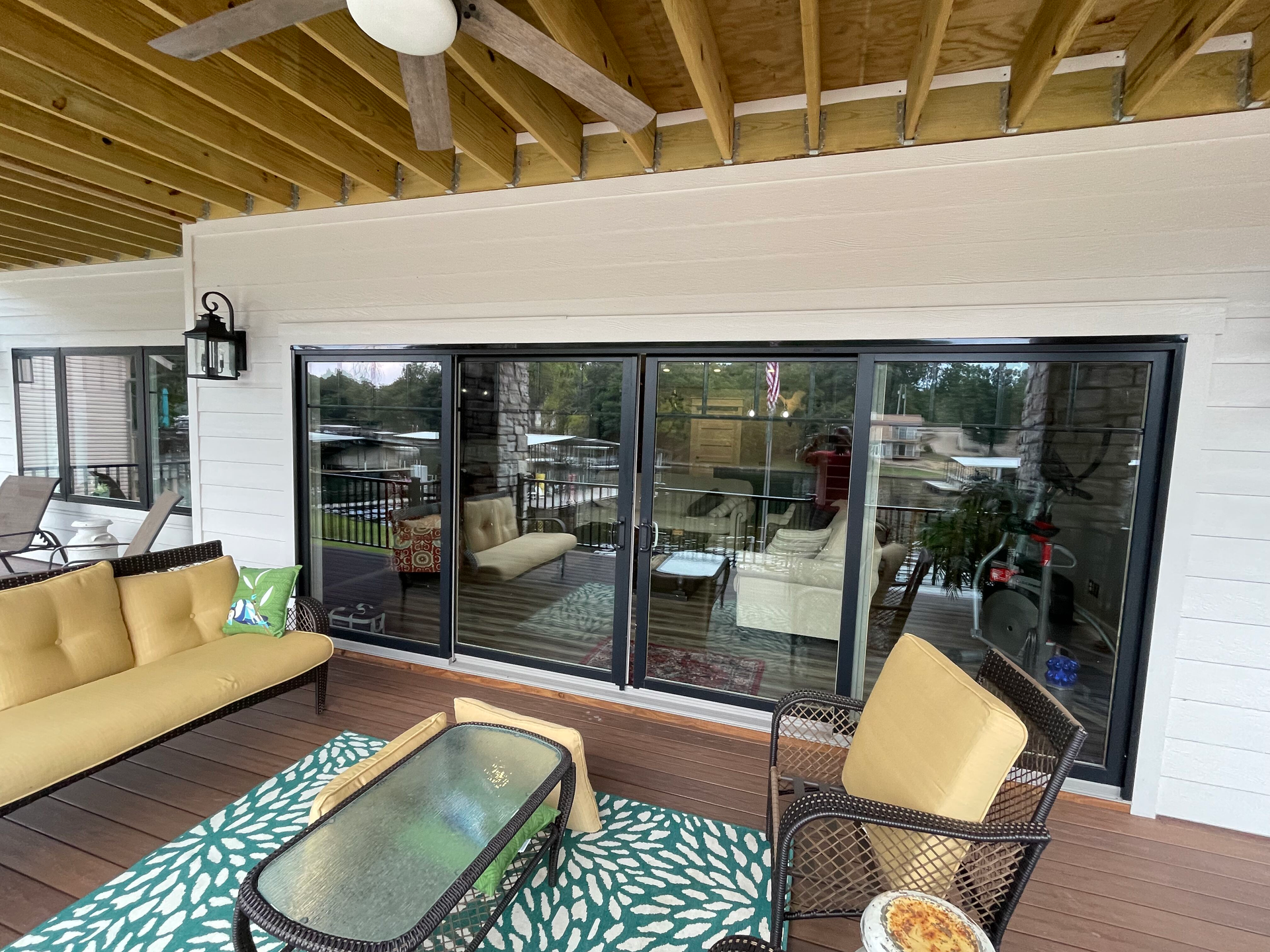 Patio with tan sofa, glass coffee table, chairs, and sliding glass doors under a wood ceiling