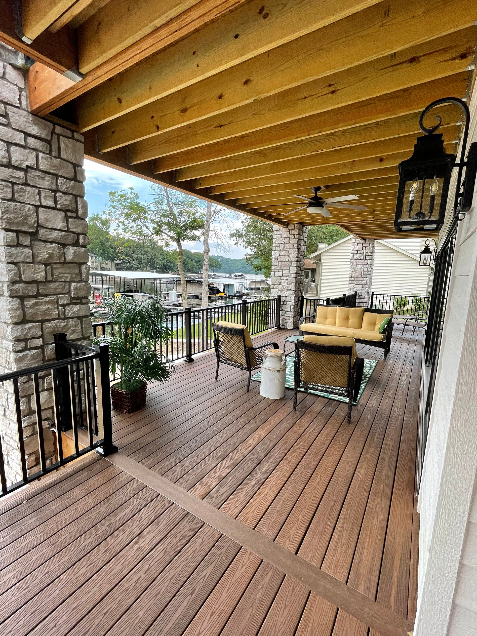 Covered wooden porch with picnic table, hanging lantern, and brick columns overlooking a street.