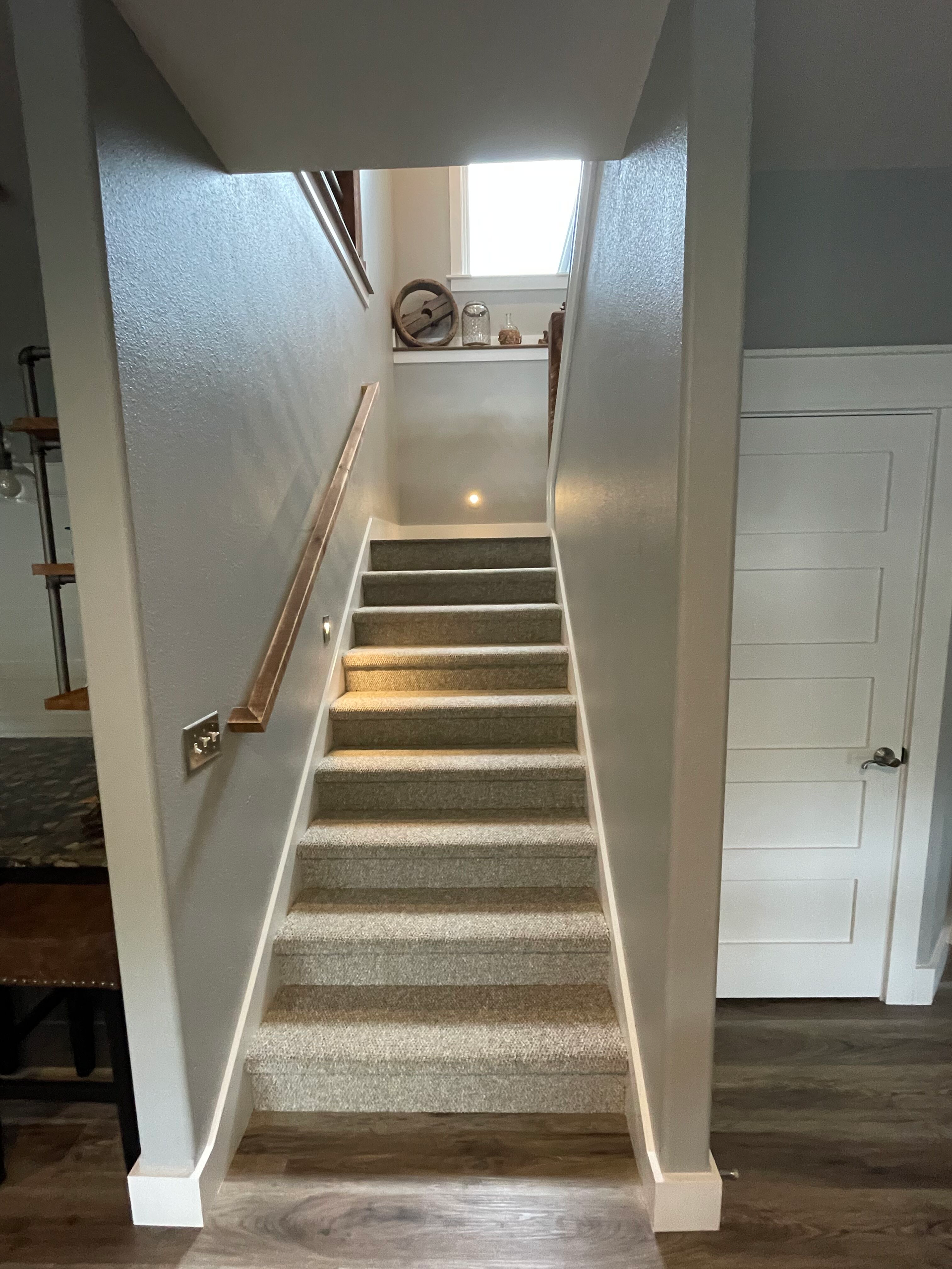 Carpeted staircase with wooden handrail leading to a bright upstairs landing.