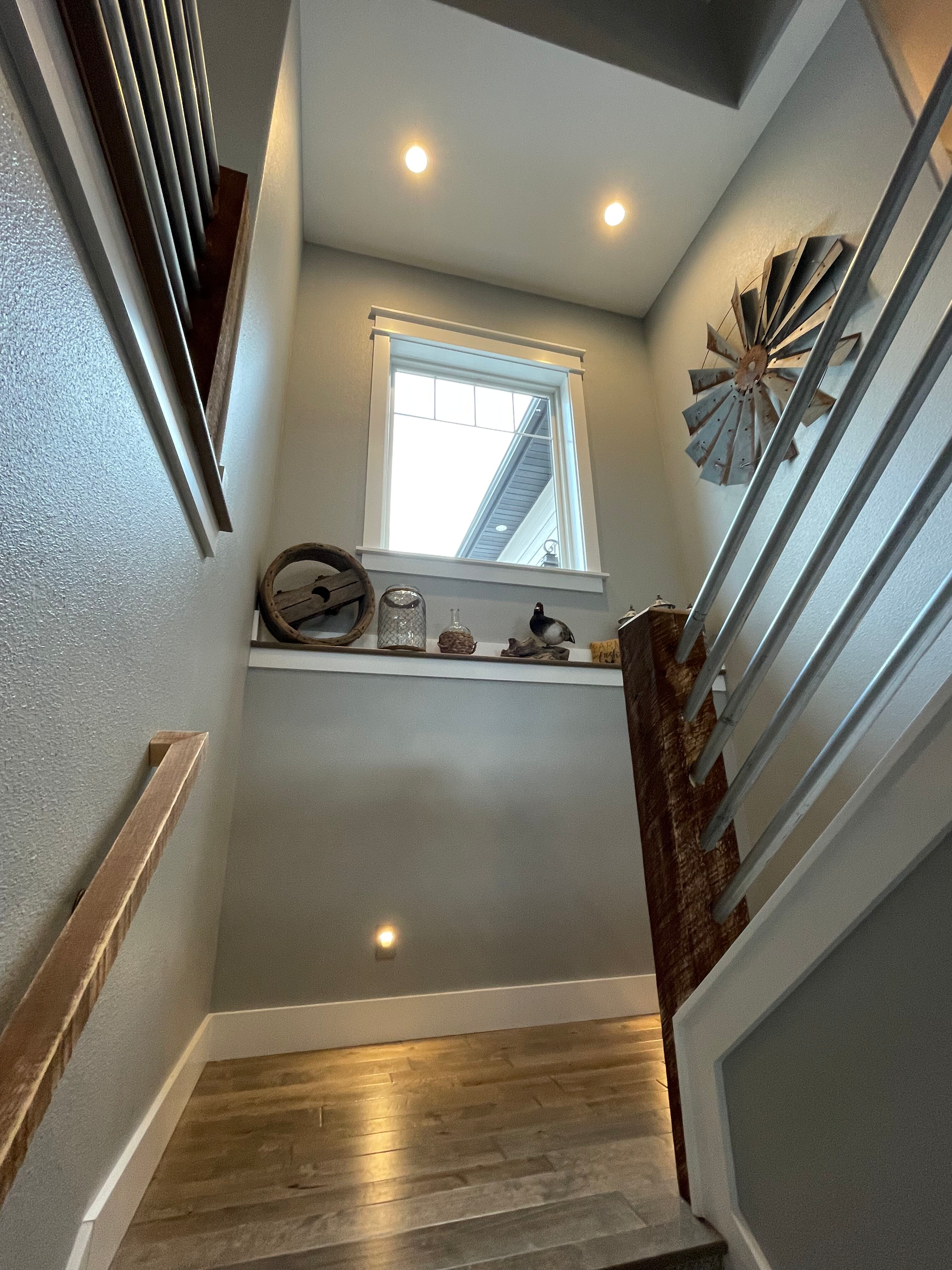 Narrow stairwell with wooden steps, gray walls, skylight window, and recessed ceiling lights.
