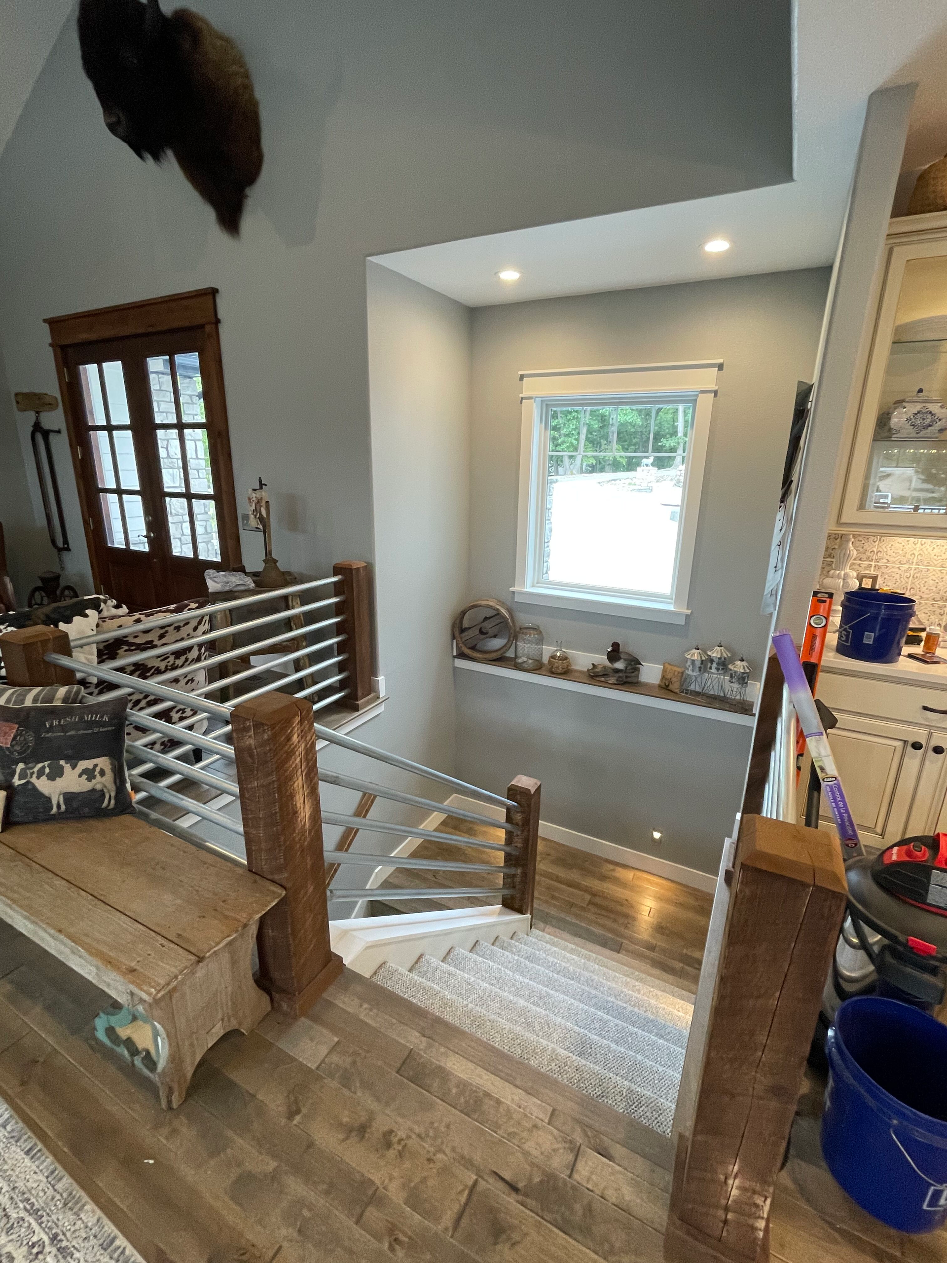 Stair landing with wood floor, cable railing, window seat, and blue bucket in a bright home interior