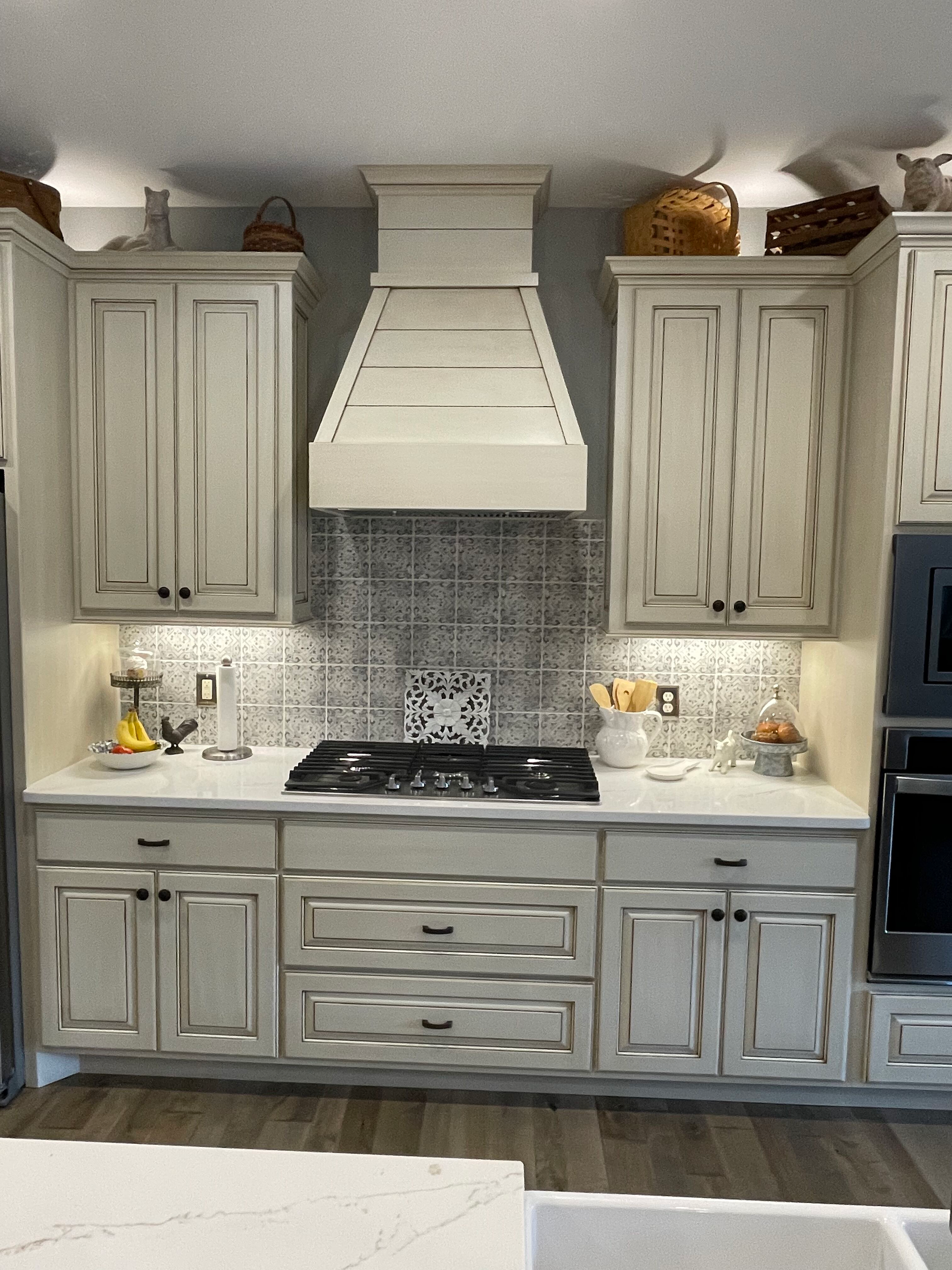 White kitchen with distressed cabinets, marble-look backsplash, and a centered range hood.