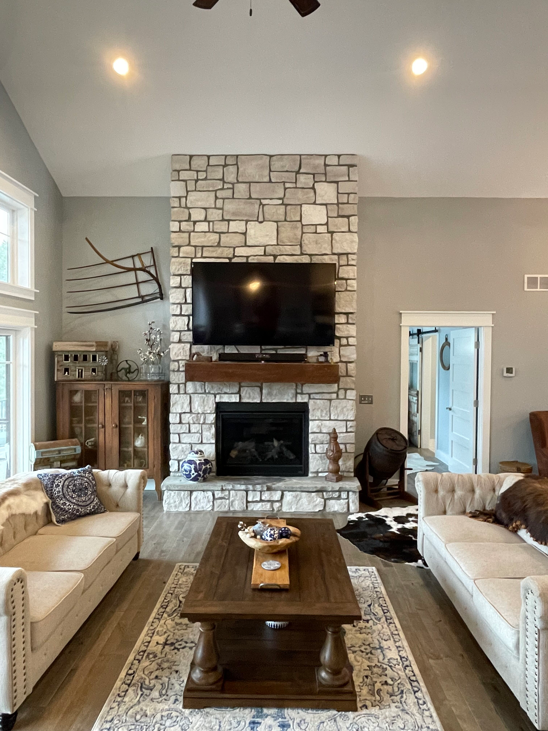 Spacious living room with stone fireplace, TV, beige sofas, and wooden coffee table centered on a patterned rug.
