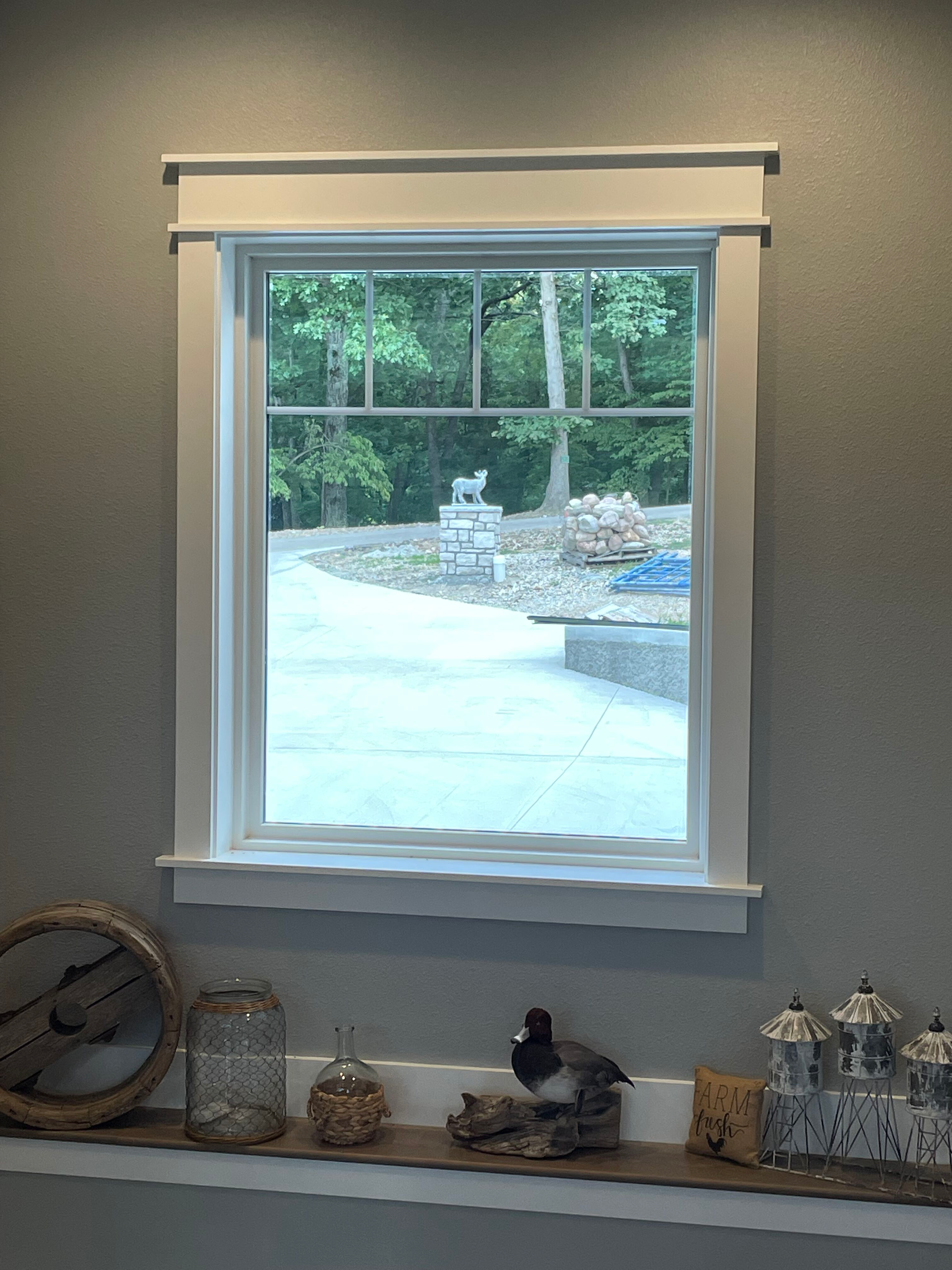 Window with white trim and shade overlooking a snowy yard, with small decor items on the sill below.