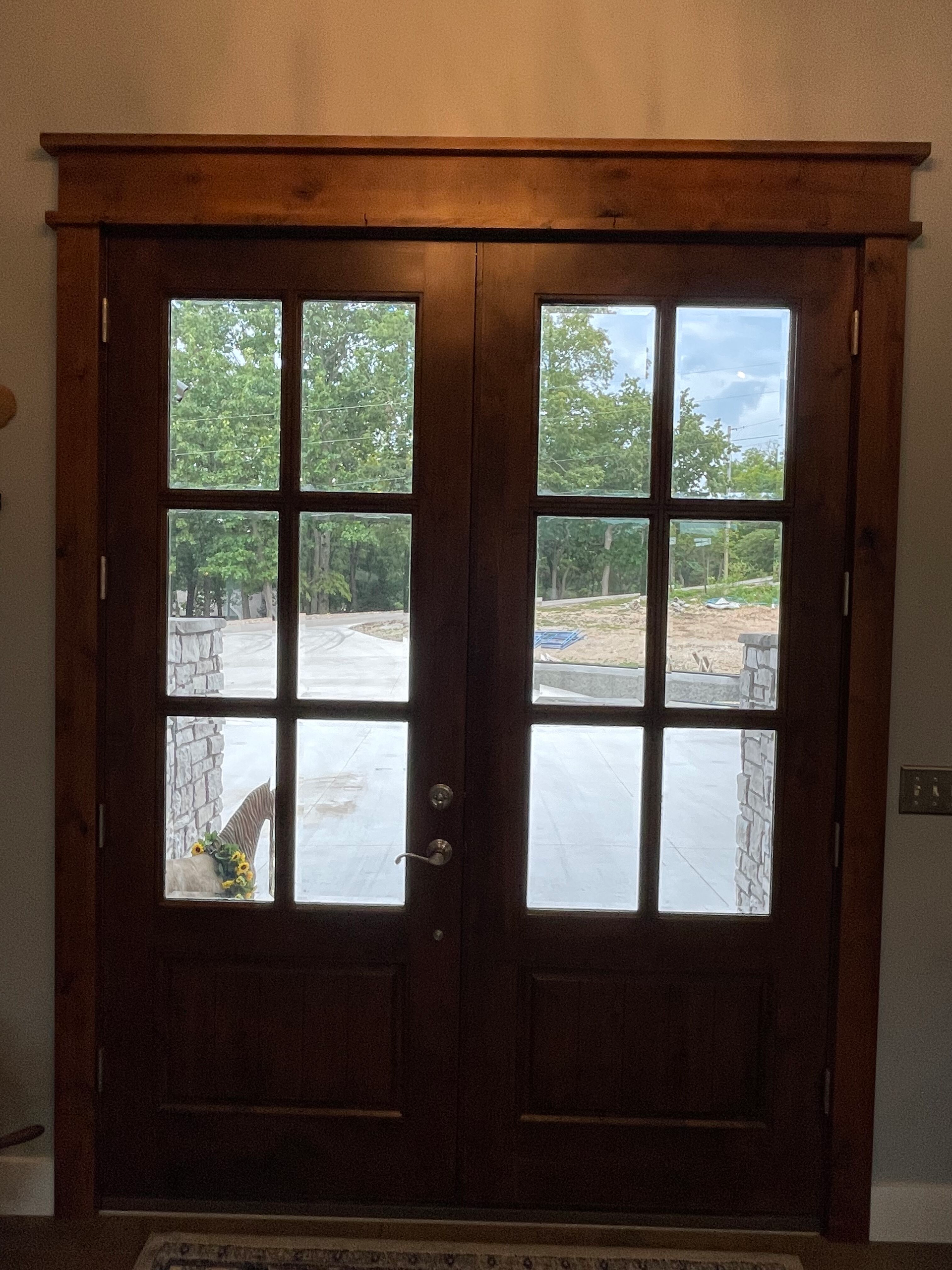 Wooden double front doors with glass panes, showing a bright outdoor view beyond.