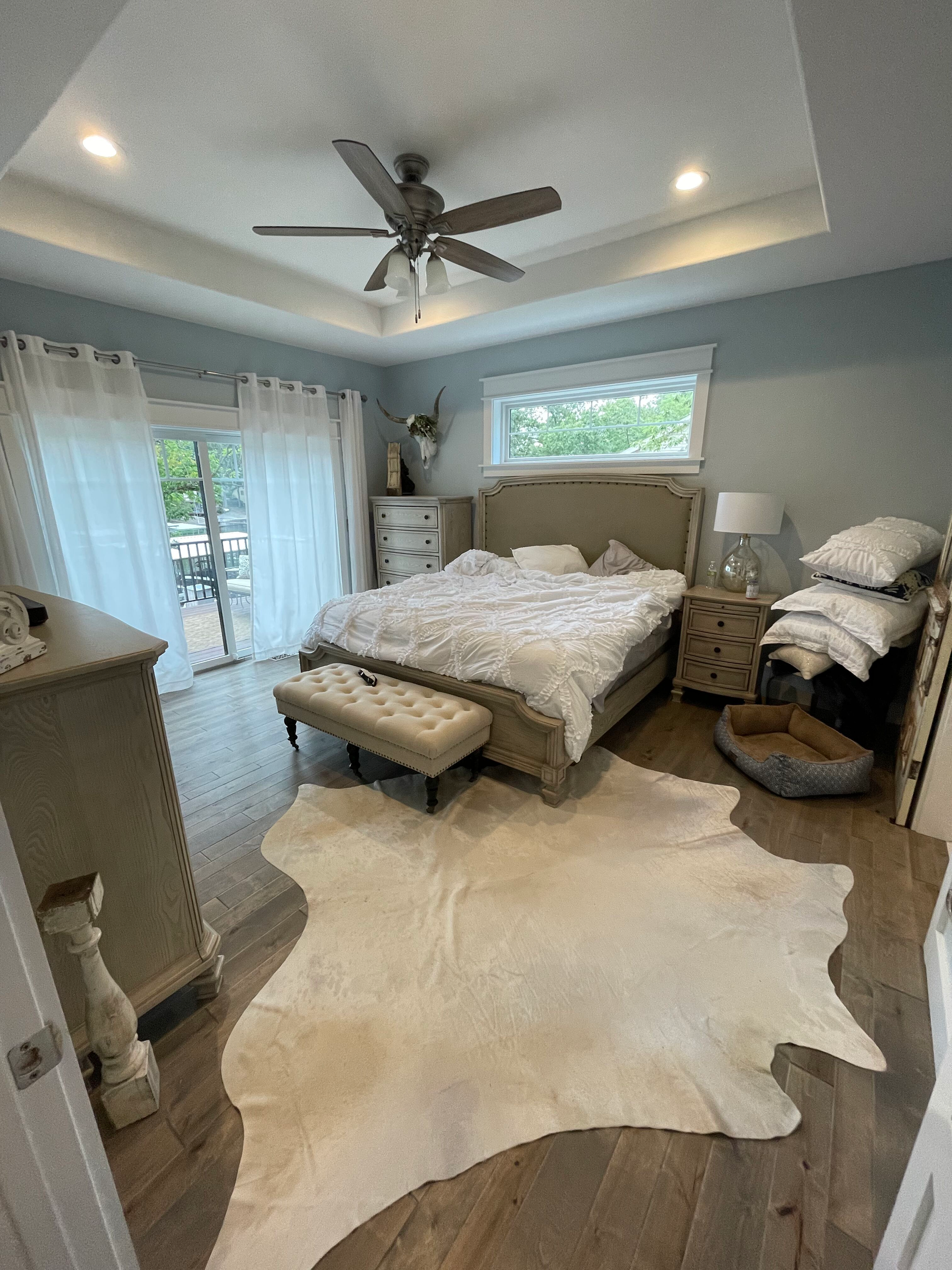 Bright bedroom with a bed, ceiling fan, window, white rug, and dresser in soft gray tones