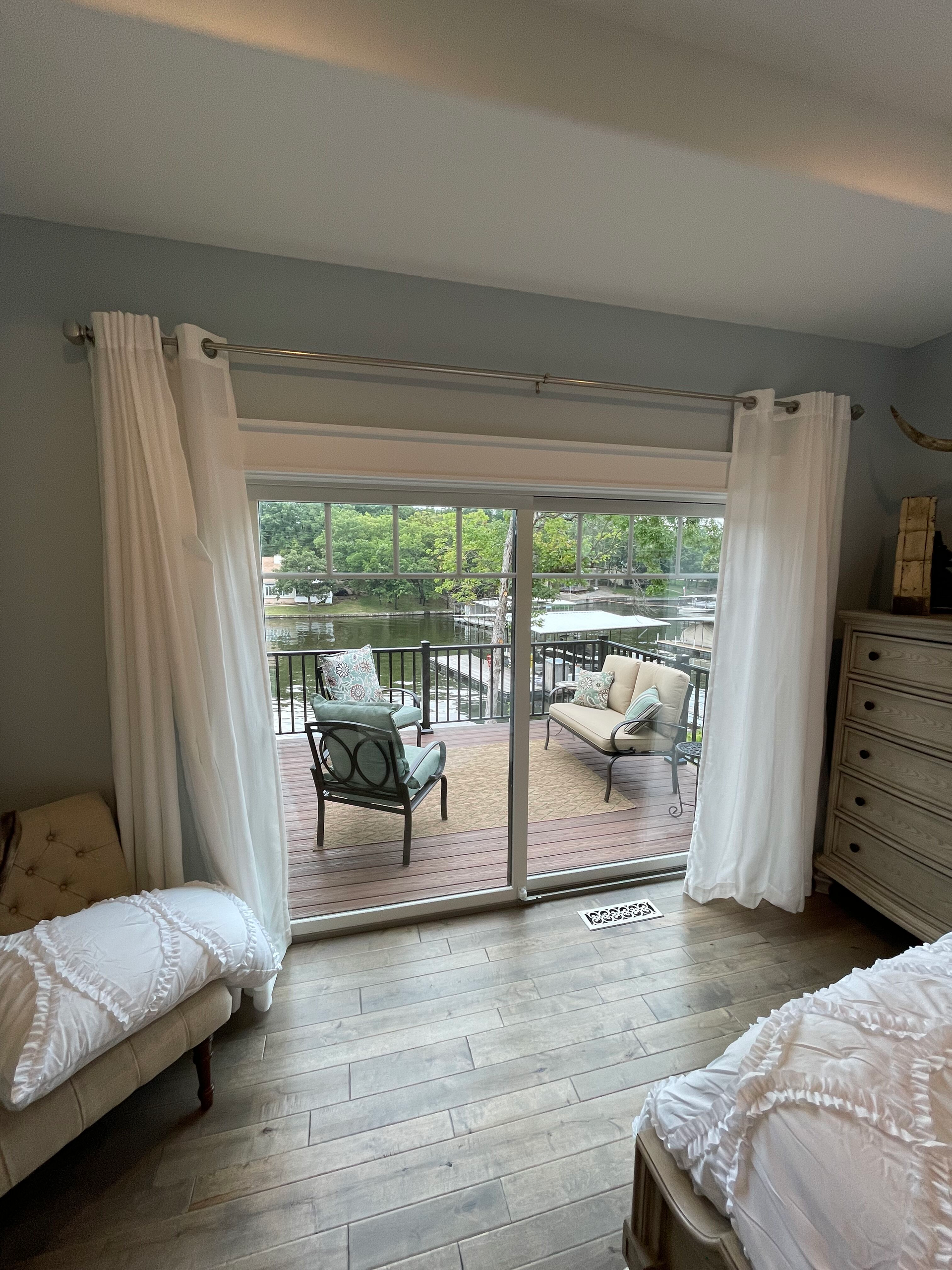 Bright bedroom with sliding glass doors opening to a patio, white curtains, and a bed in the foreground.