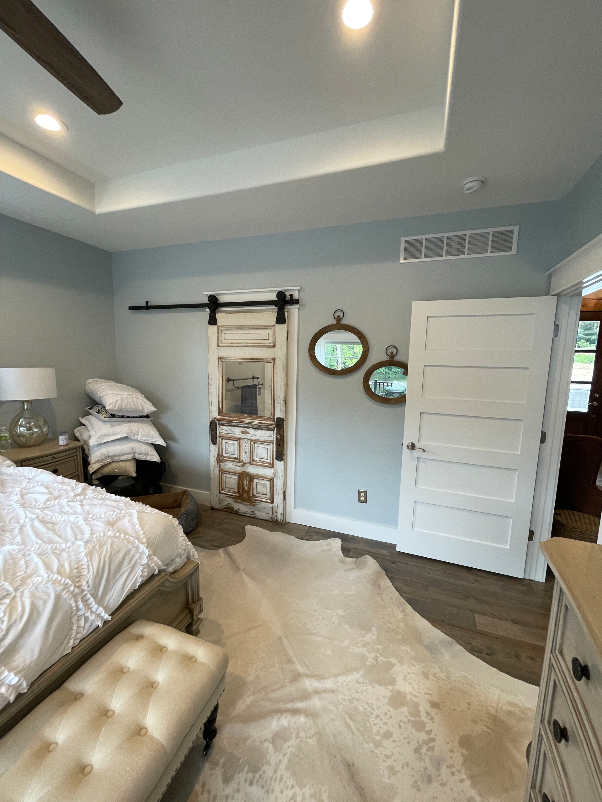 Bright bedroom with white bed, cream rug, sliding barn door, and wall mirrors on pale blue walls.