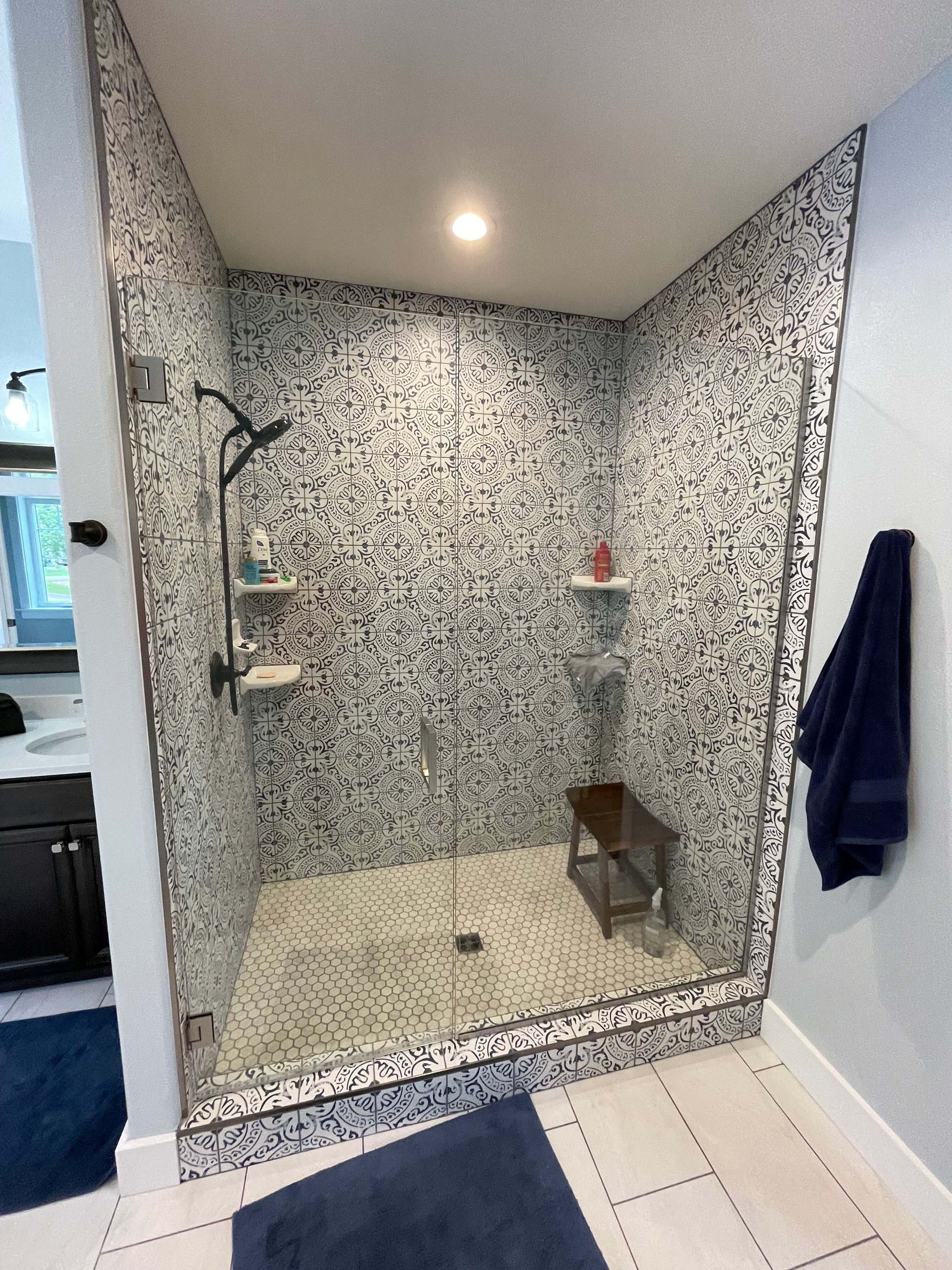 Tiled walk-in shower with speckled walls, rainfall showerhead, and white mosaic floor