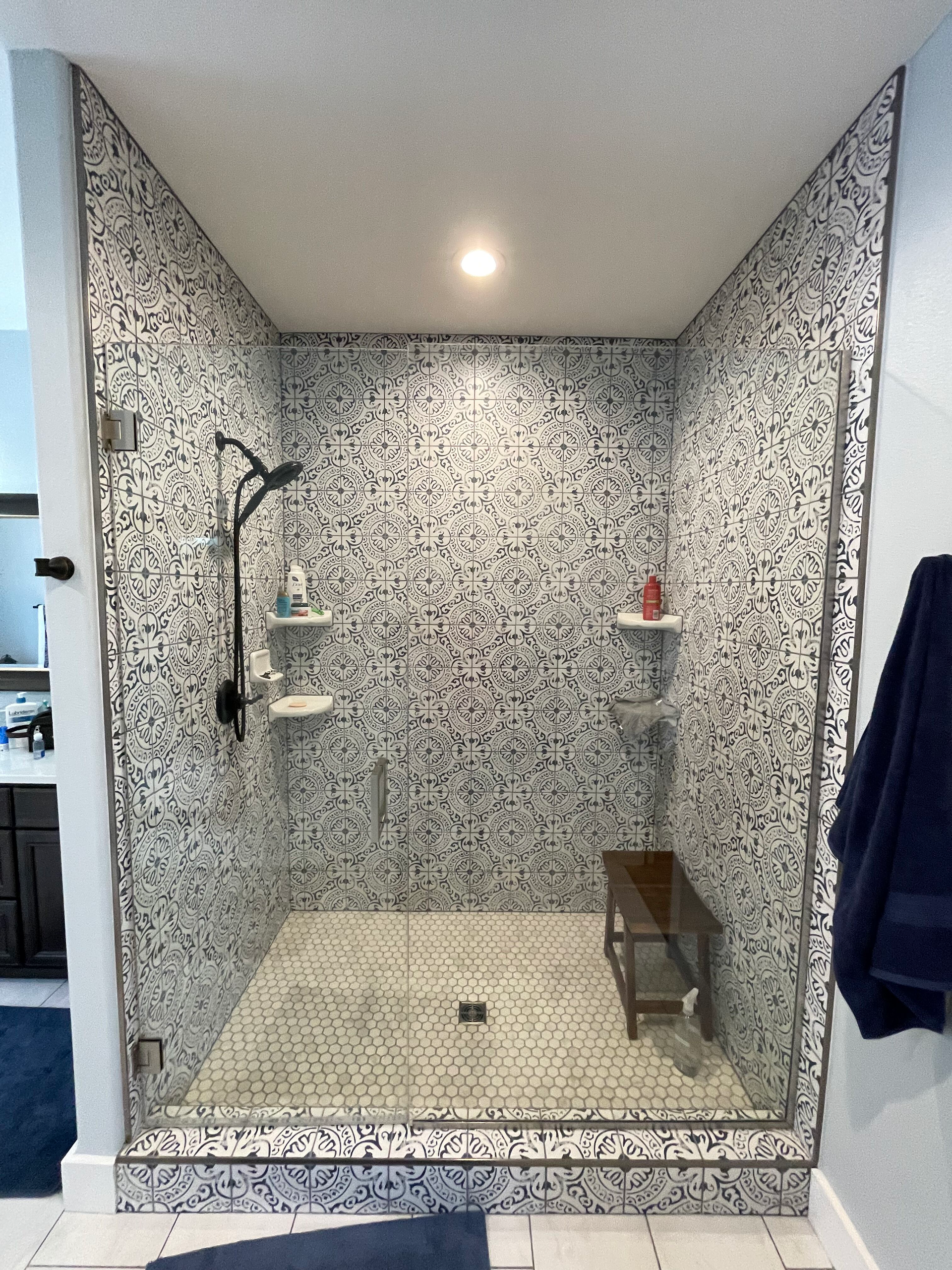 Walk-in shower with mosaic tile walls, rainfall showerhead, shelf, and towel hanging on the right.
