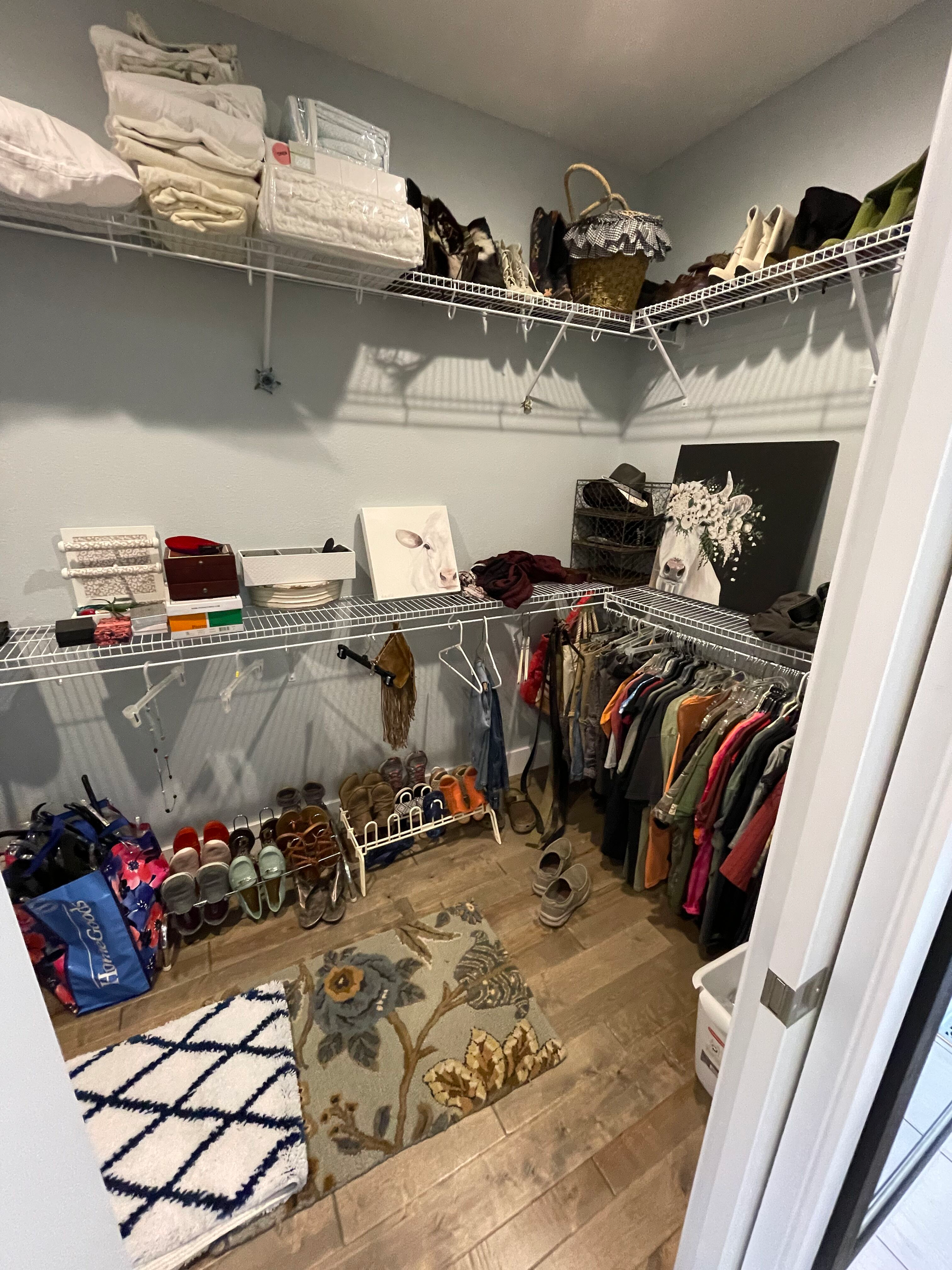 Walk-in closet with wire shelves, hanging clothes, shoes, hats, and folded linens on a wood floor.