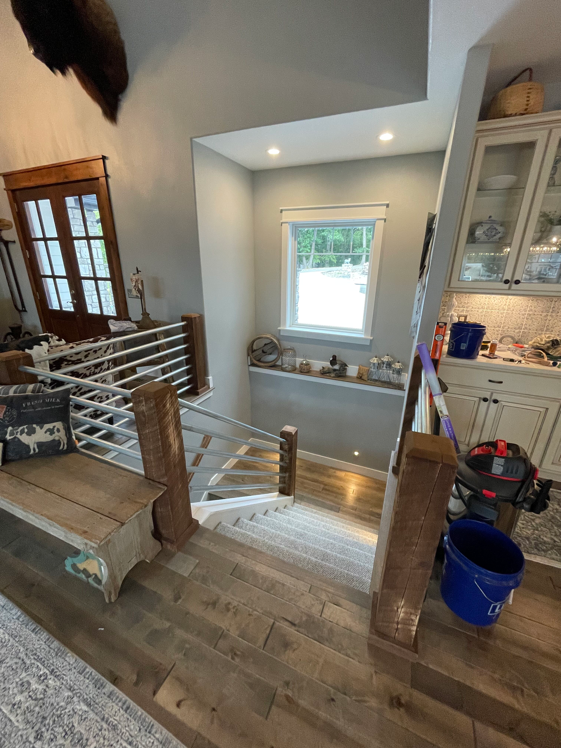Stair landing with wooden railings, window seat, glass cabinet, and a light wood floor in a bright home interior