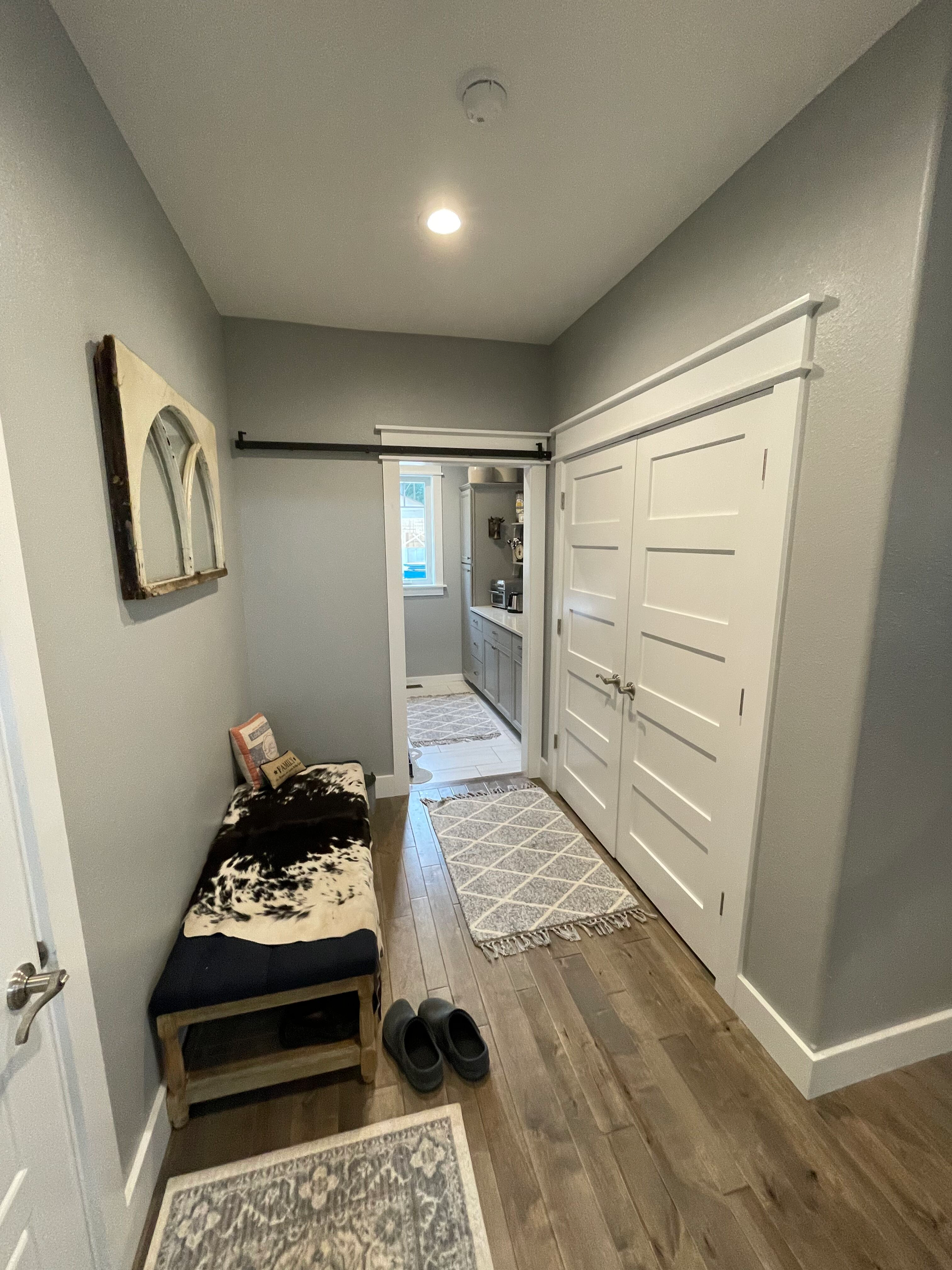 Narrow hallway with gray walls, wood floor, bench, rug, and white sliding closet doors leading to a bright room