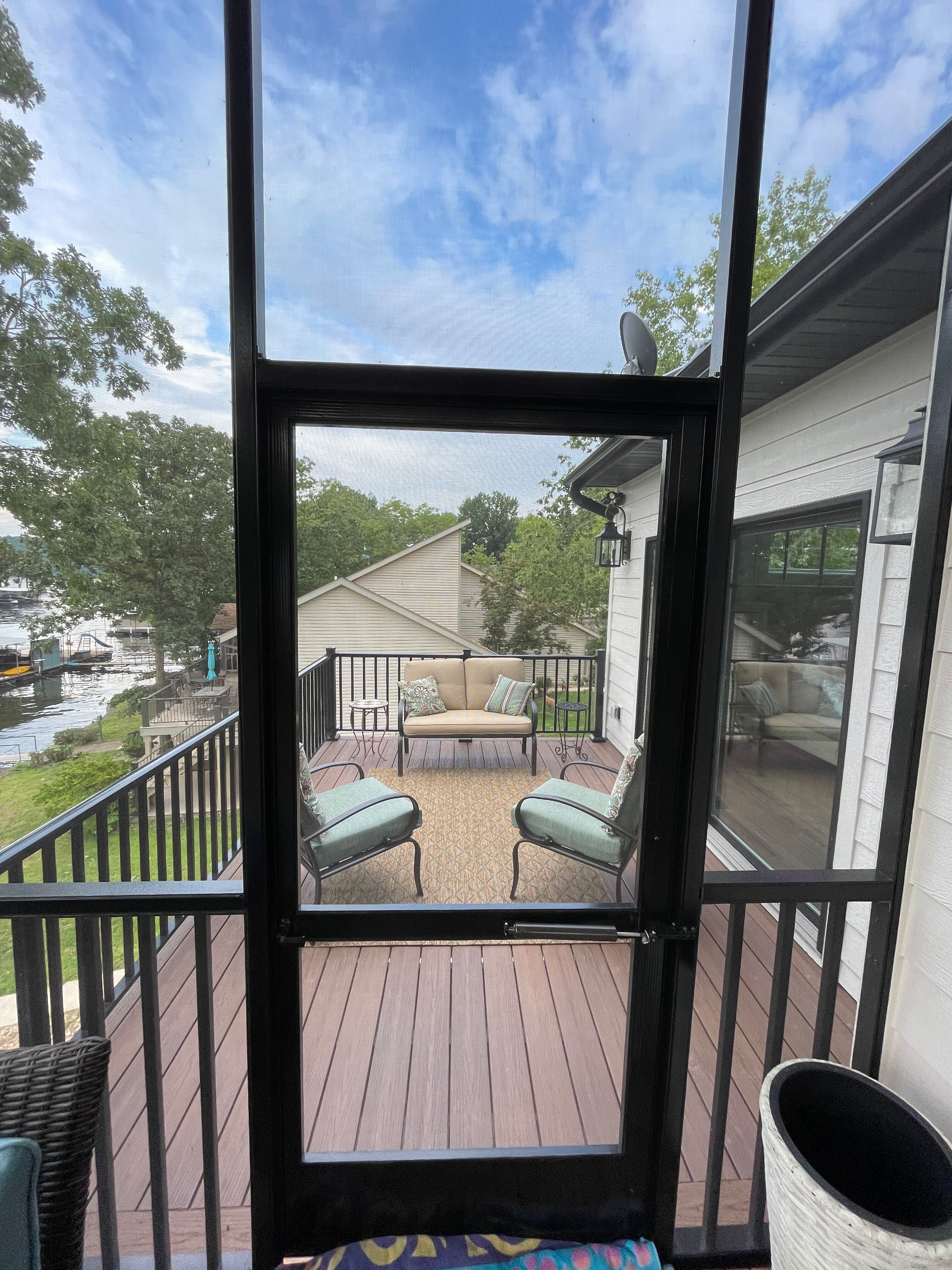 Covered porch with two teal chairs, a small table, and a view of the lake and neighboring homes.