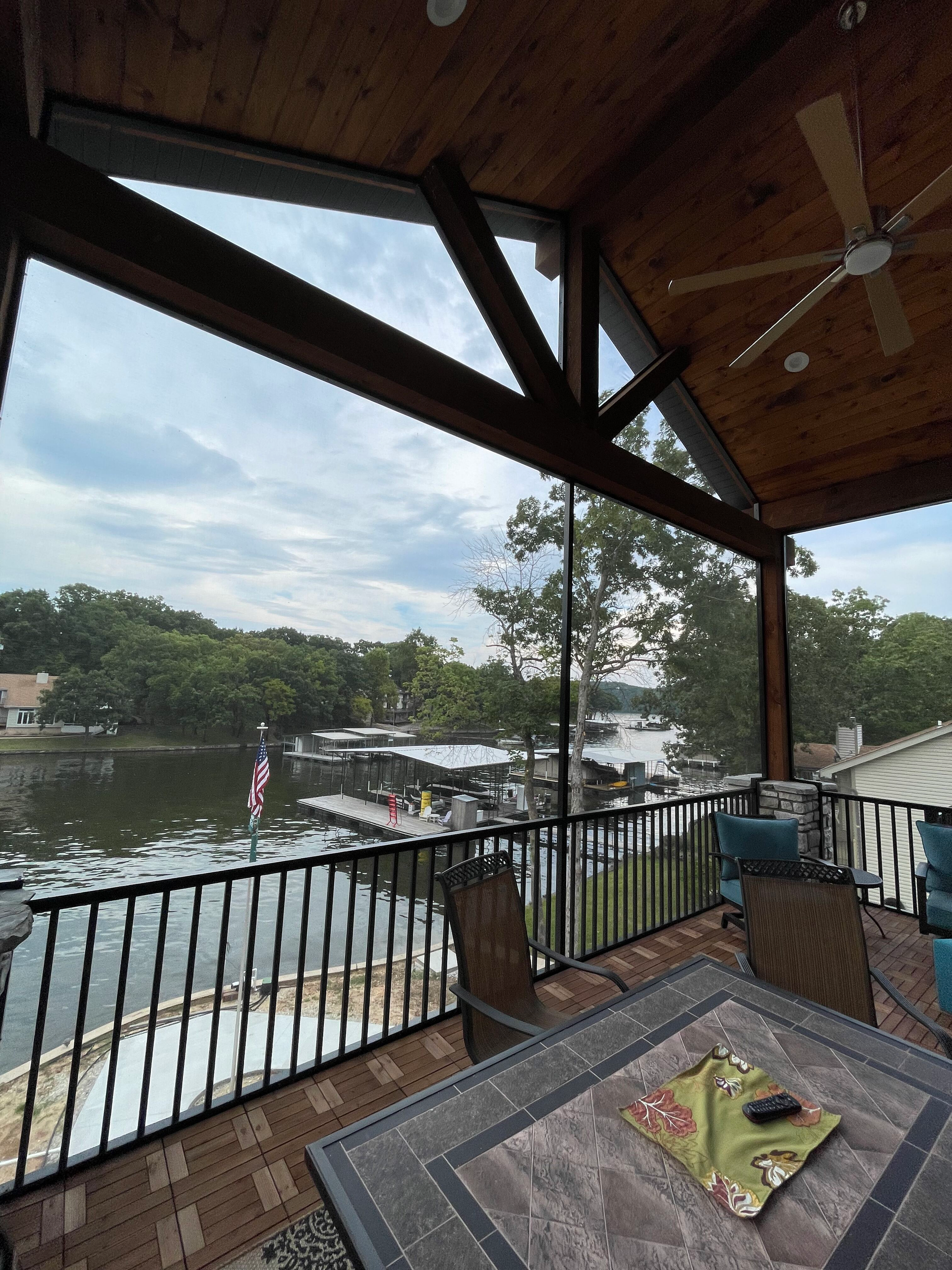 Covered patio overlooking a river with boats, railings, and a cloudy sky over green trees.