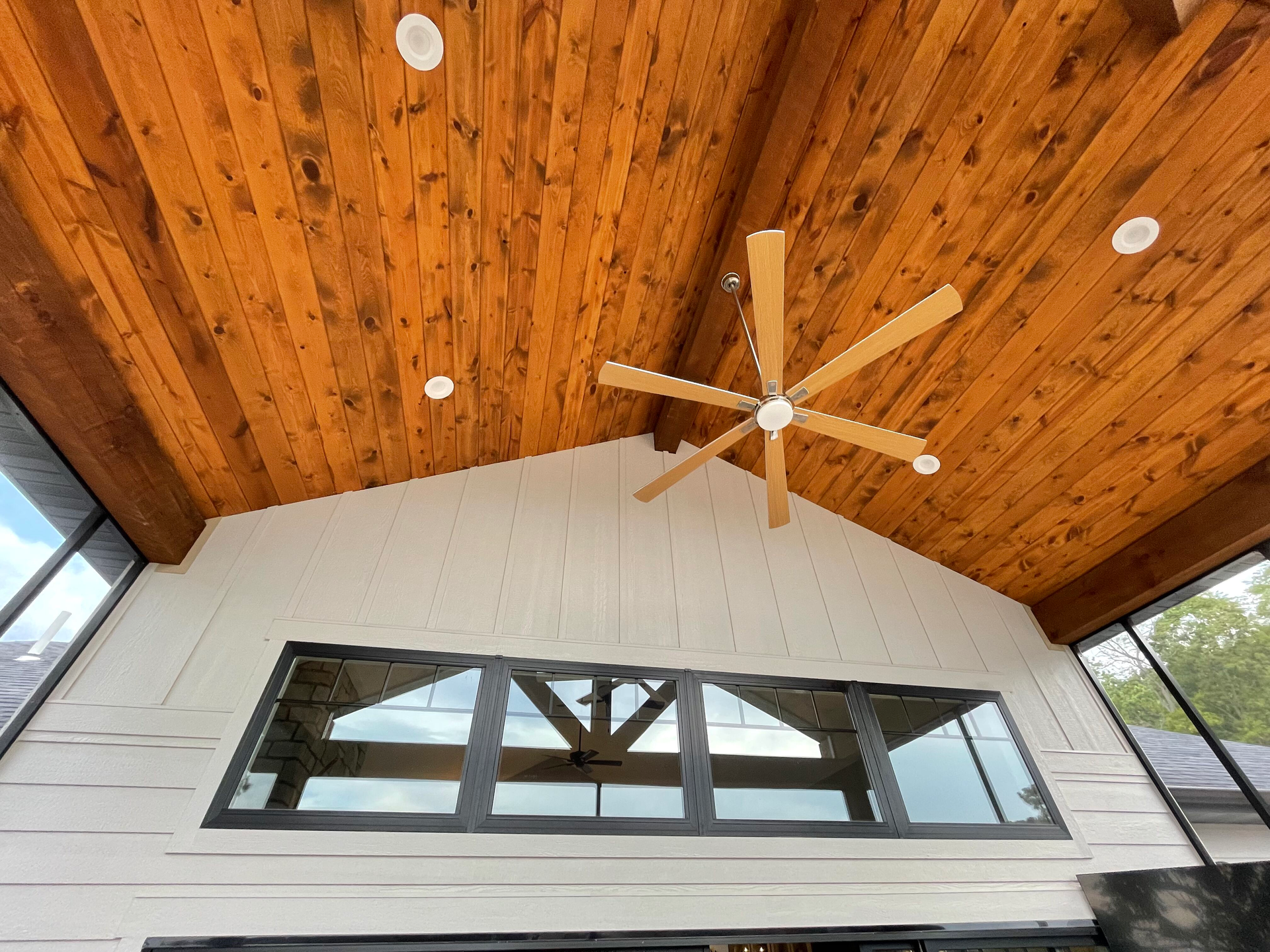 Vaulted white porch ceiling with wood planks, ceiling fan, and wide windows above a wall.
